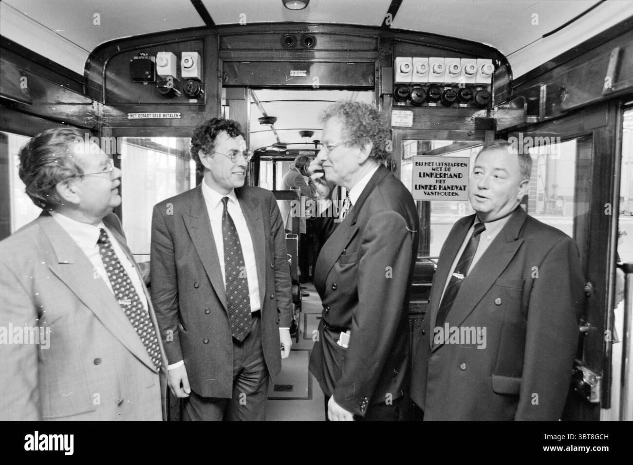 Tram restaurati per Rotterdam, Whizgle News, Dutch Desk, Paesi Bassi, 1950 - 2000 il 11-05-2000. L'immagine include questi argomenti. In un abitacolo ben illuminato di un tram, un gruppo di quattro uomini si mette insieme, impegnati in una conversazione. L'ambiente trasmette un senso di nostalgia, con pannelli in legno lucido e finiture vintage. Gli uomini sono vestiti con abiti formali; abiti in tonalità grigio scuro e blu scuro, completi di cravatte, che contribuiscono a creare un ambiente professionale. Le loro espressioni vanno dal serio all'amabile, suggerendo una discussione vivace. Dietro di loro, le finestre del tram rivelano un indizio sfocato Foto Stock