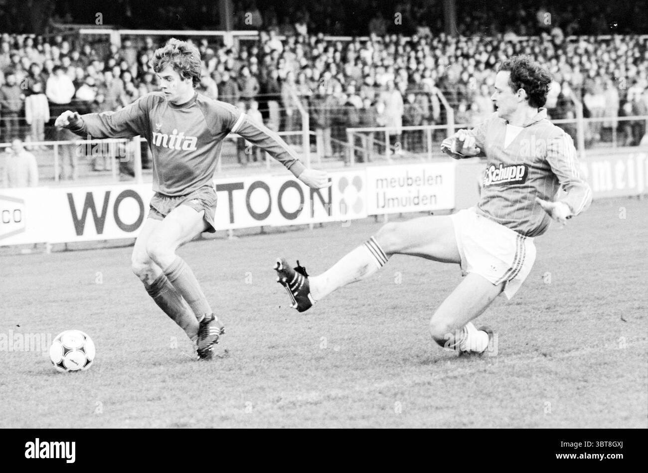 Partita di calcio HFC Haarlem - PEC Zwolle., Whizgle News, Dutch Desk, Paesi Bassi, 1950 - 2000. Questi sono gli argomenti nell'immagine. La scena cattura un momento intenso su un campo di calcio erboso, dove due giocatori sono impegnati in una partita competitiva. Un giocatore, indossando una maglia di colore arancione brillante, manovra abilmente la palla, mostrando agilità e concentrazione. La sua espressione riflette la determinazione, evidenziando l'intensità del gioco. Il secondo giocatore, rivestito con una maglia altrettanto vivace ma di colori diversi, si trova in posizione difensiva, preparandosi ad intercettare l'azione in arrivo. Il suo corpo Foto Stock