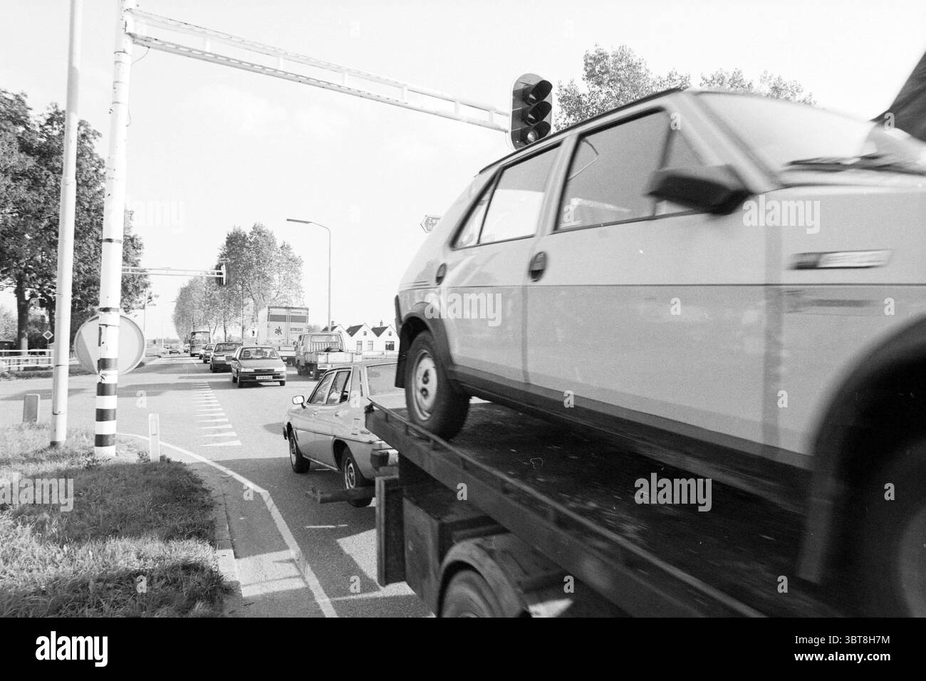 Incrocio IJweg Oude Schipholweg. Costruzione di strade messa in strada Boesingheliede IJweg, Whizgle News, Dutch Desk, Paesi Bassi, 1950 - 2000 il 04-10-1989. Questi argomenti sono mostrati nell'immagine. La scena rivela una strada movimentata, catturata in bianco e nero, che la impreziosisce di un'atmosfera classica e un po' nostalgica. Sul fronte, un camion trasporta un'auto di colore chiaro, visibilmente fissata sul pianale; l'auto si distingue contro le sfumature più profonde del veicolo. A sinistra, un'intersezione circolare conduce l'occhio sullo sfondo, con diversi veicoli posizionati a varie angolazioni, su Foto Stock