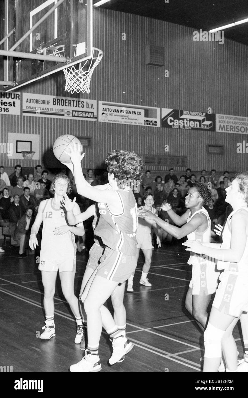 Basket Lisse - Akrides Ladies, Whizgle News, Dutch Desk, Paesi Bassi, 1950 - 2000 il 19-01-1991. Questi sono gli elementi dell'immagine. In una vivace palestra si svolge una dinamica partita di basket. L'attenzione è incentrata su un giocatore che indossa una maglia rossa brillante, che è in volo, pronto a fare un tiro. I suoi capelli ricci girano verso l'esterno mentre cattura la palla in alto sopra la testa, trasudando energia e determinazione. Intorno a lei, diversi avversari in uniforme bianca si scontrano difensivamente, con un giocatore che estende le braccia nel tentativo di bloccare il colpo. La scena è piena di azione, con i giocatori Foto Stock