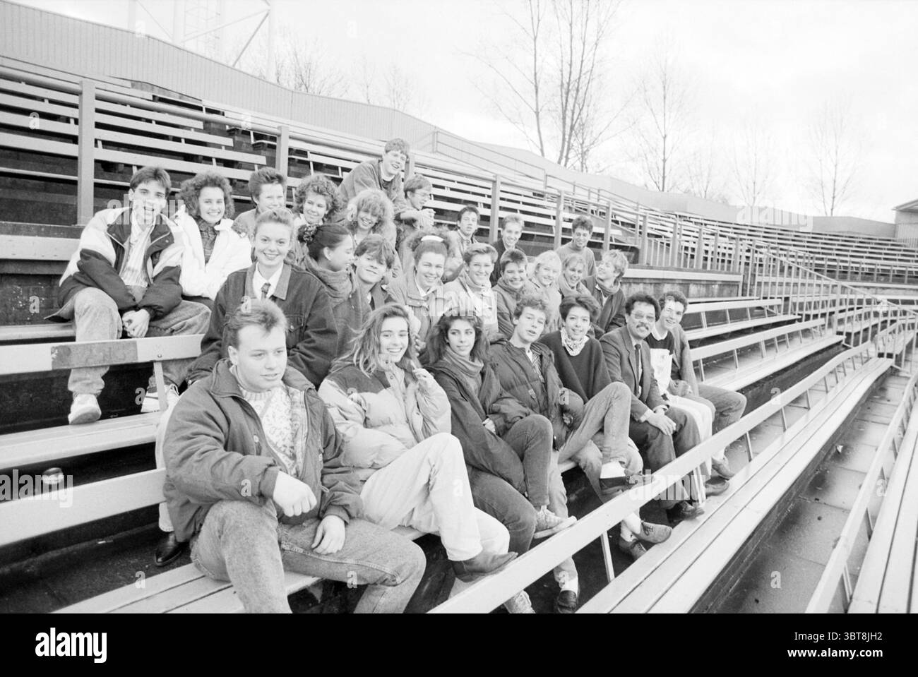 Corso sul giornale Mendellschool gruppo 4 HAVO Schools, Whizgle News, Dutch Desk, Paesi Bassi, 1950 - 2000 il 19-12-1988. L'immagine include questi argomenti. La scena presenta un gruppo di individui seduti in una disposizione semicircolare su una serie di sbiancanti, che sono fatti di metallo e legno. L'atmosfera generale e' informale e trasmette un senso di cameratismo tra le persone. Gli individui sono vestiti con un mix di stili di abbigliamento tipici tra la fine degli anni '80 e l'inizio degli anni '90, con molti che indossano giacche oversize, maglioni e camicie casual. Alcuni hanno acconciature ricci e voluminose, mentre altri Foto Stock