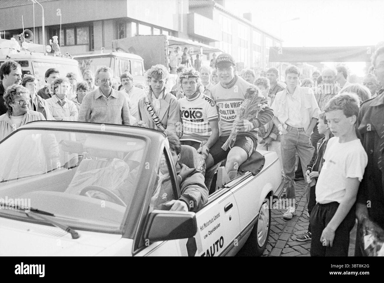 Vincitori dell'IJmuiden Cycling tour Cycling IJmuiden Paesi Bassi, Whizgle News, Dutch Desk, Paesi Bassi, 1950 - 2000 il 23-06-1985. L'immagine contiene questi argomenti. La scena cattura un'atmosfera vivace e vivace, incentrata su una cabriolet. Contro il veicolo c'è un gruppo di ciclisti, vestiti con vivaci maglie da corsa, adornati da vari loghi e sponsorizzazioni. Le loro espressioni irradiano entusiasmo e successo, suggerendo che hanno appena completato una gara o un evento significativo. La folla che li circonda è variegata e comprende spettatori di età e età diverse Foto Stock