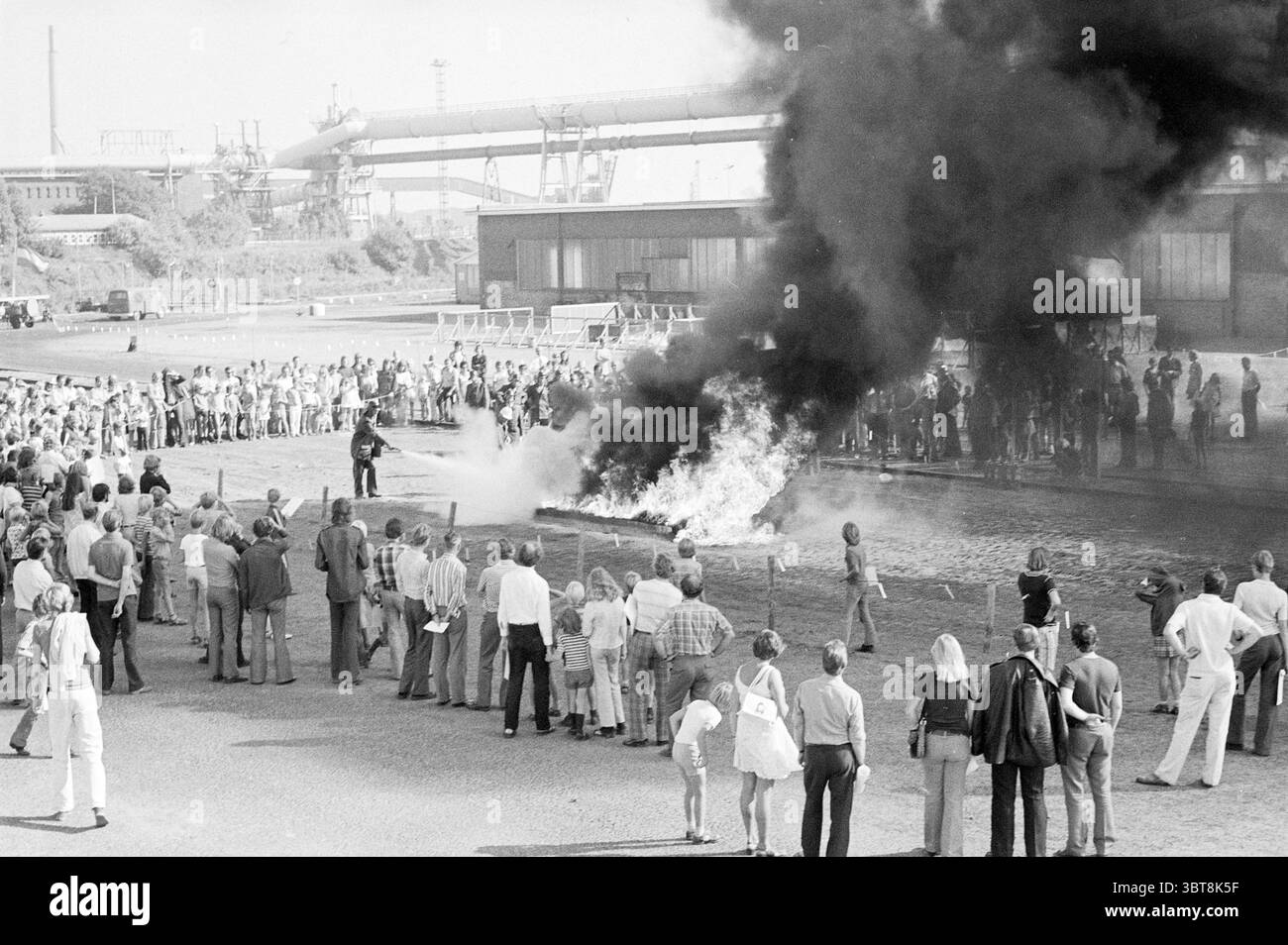 Vigili del fuoco giorno altiforni antincendio, Whizgle News, Dutch Desk, Paesi Bassi, 1950 - 2000 il 08-09-1973. L'immagine include questi argomenti. La scena cattura un momento drammatico in cui un fuoco significativo emette fitti pennacchi di fumo nero, che si arricciano verso il cielo. Le fiamme sfarfallio energico, contrastando nettamente con le nuvole più scure di fumo. Intorno al fuoco, si raduna una grande folla di persone, mostrando una varietà di reazioni che vanno dallo shock alla curiosità. Il pubblico è composto da diversi individui, alcuni vestiti con abiti estivi più leggeri, inclusi Foto Stock