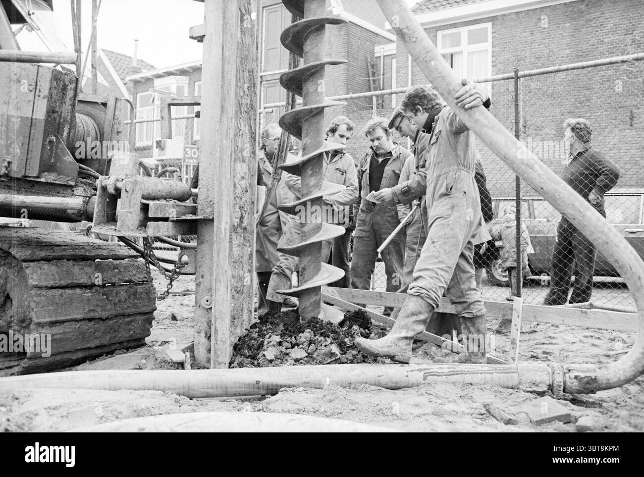 Primo mucchio per case sul primo mucchio Herensingel Haarlem Herensingel Paesi Bassi, Whizgle News, Dutch Desk, Paesi Bassi, 1950 - 2000 il 30-01-1981. Questi argomenti vengono visualizzati nell'immagine. La scena ritrae un gruppo di individui impegnati in un'operazione di perforazione. Centrato nella composizione è una grande perforatrice, dotata di una coclea sporgente che scorre verso il basso nel terreno. Il macchinario ha un aspetto robusto e industriale, con una texture resistente agli agenti atmosferici che ne indica l'uso intensivo. Attorno al macchinario, diverse persone sono riunite da vicino, a dimostrazione dello sforzo collaborativo. Sono d Foto Stock