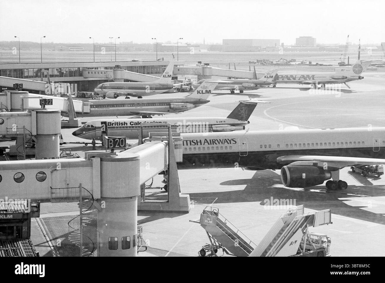 Aerei in attesa a Schiphol Schiphol Schiphol, Whizgle News, Dutch Desk, Paesi Bassi, 1950 - 2000 il 17-03-1988. L'immagine include questi argomenti. La scena cattura un vivace terminal dell'aeroporto visto da un punto panoramico elevato. Una varietà di aerei sono parcheggiati ai cancelli, ciascuno decorato con una livrea di compagnie aeree distinta. Notevole tra questi è un jet della British Airways con i suoi iconici accenti blu scuro e rosso, in piedi vicino a un aereo della Caledonia britannica caratterizzato da una caratteristica tavolozza di colori verde e bianco. L'aereo KLM completamente bianco e il jet Pan Am retrò, noto per il suo glo blu brillante Foto Stock