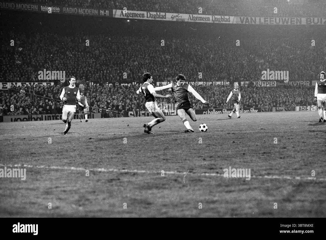 Feyenoord - Kaiserslautern Football Feyenoord, Whizgle News, Dutch Desk, Paesi Bassi, 1950 - 2000 il 03-11-1976. Questi argomenti vengono visualizzati nell'immagine. La scena cattura un momento di tensione su un campo di calcio, dove i giocatori sono pienamente impegnati nell'azione. In primo piano, un giocatore che indossa una maglia scura manovra abilmente la palla, mostrando un'espressione mirata mentre si prepara a fare un gioco decisivo. La sua postura è dinamica, con una gamba allungata e la palla posizionata poco più avanti, mostrando un momento di atletismo. Nelle vicinanze, un'altra persona con una maglia di colore chiaro sta premendo in avanti, a temperatura Foto Stock