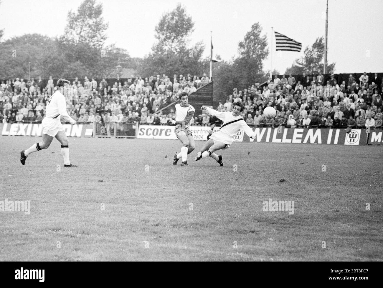 OG - Bloemendaal Voetbal VV Schoten Onze Gezellen Renova, Whizgle News, Dutch Desk, Paesi Bassi, 1950 - 2000 il 21-09-1969. Questi sono gli argomenti nell'immagine. La scena cattura un momento intenso su un campo da calcio erboso, dove si sta svolgendo un gioco dinamico. Un gruppo di spettatori riempie lo sfondo, le loro figure leggermente sfocate, indicando una grande folla coinvolta nell'azione. I tifosi dimostrano un'ampia gamma di emozioni, dall'emozione all'attesa, mentre guardano la partita svolgersi. In primo piano, due giocatori sono in primo piano. Uno è in maglia a righe, manovre sapientemente Foto Stock