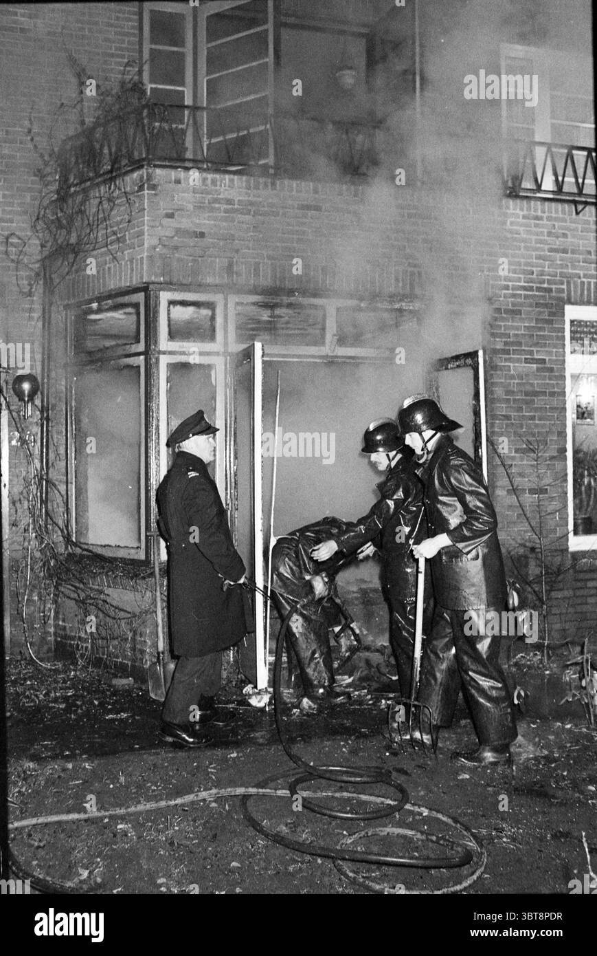 Fire Zandvoorter Allee spara i vigili del fuoco Haarlem Zandvoorter Allee Paesi Bassi, Whizgle News, Dutch Desk, Paesi Bassi, 1950 - 2000 il 02-12-1982. L'immagine include questi argomenti. La scena raffigura un'intensa risposta di emergenza a un incendio. In primo piano, diversi vigili del fuoco vestiti con equipaggiamento e caschi di protezione oscuri stanno lavorando attivamente per controllare il fuoco. Sono posizionati vicino a una porta che conduce all'interno di un edificio in mattoni, parzialmente oscurato dal fumo che fuoriesce nell'aria. L'esterno in mattoni della struttura ha un aspetto resistente agli agenti atmosferici, con alcune aree visibilmente c Foto Stock