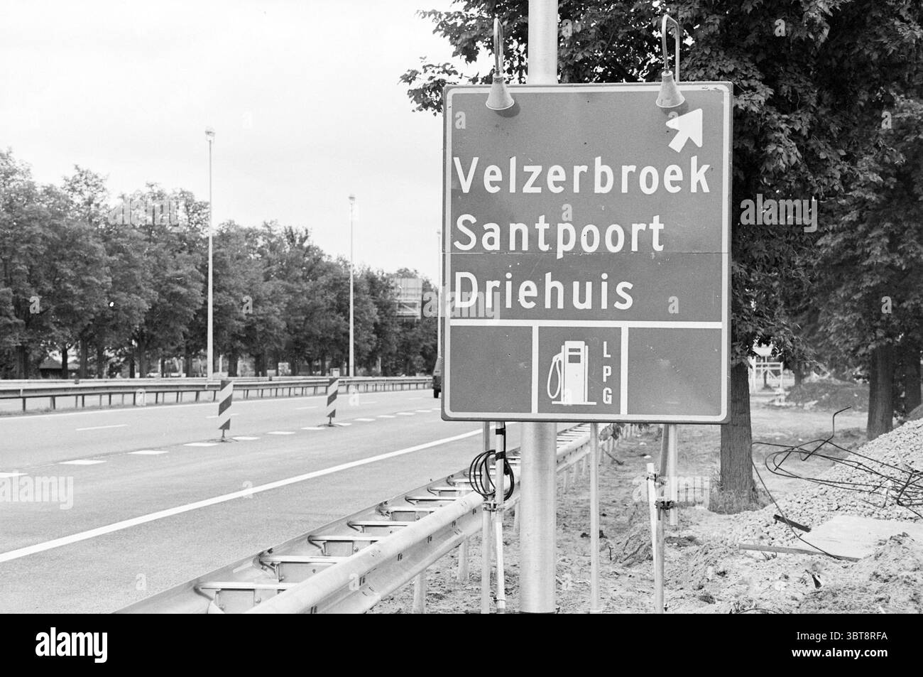 Cartello Velzerbroek, Whizgle News, Dutch Desk, Paesi Bassi, 1950 - 2000 nel 1993. Questi argomenti vengono visualizzati nell'immagine. Nella scena, un grande segno rettangolare è ben visibile sul lato di una strada, indirizzando i conducenti verso le posizioni vicine. Il cartello è delimitato da una struttura metallica e posizionato ad angolo, suggerendo la sua importanza per la navigazione nell'area. Lo schema di colori consiste principalmente in blu intenso e bianco, creando un contrasto netto che attira l'attenzione. Intorno al cartello, l'ambiente presenta un ampio marciapiede che conduce a una carreggiata con segni chiari, forse indicati Foto Stock