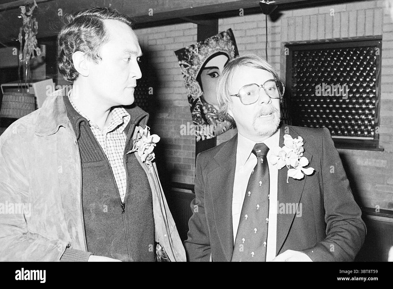 Presentazione del nuovo album Jack Jersey in Laren Persons canto e musica presentazione, Whizgle News, Dutch Desk, Paesi Bassi, 1950 - 2000 il 19-11-1977. L'immagine mostra questi argomenti. In un ambiente interno con luce calda, due uomini sono il punto focale della scena. Lo sfondo rivela una parete di mattoni testurizzati, adornata da un'opera d'arte impressionante che presenta una faccia astratta, contribuendo alla profondità dell'ambiente. L'illuminazione è morbida ma mette in risalto i dettagli, creando un'atmosfera accogliente. Il primo uomo, a sinistra, ha un'espressione seria. Ha i capelli scuri ed è vestito con una camicia scura Foto Stock