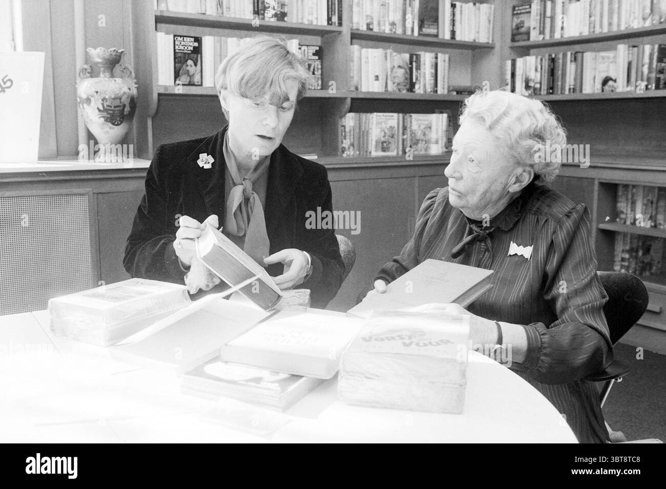 Sig.ra Gottmer con figlia in Haarlem libri e librai tipografia Haarlem Paesi Bassi, Whizgle News, Dutch Desk, Paesi Bassi, 1950 - 2000 il 11-03-1985. L'immagine contiene questi argomenti. In una stanza accogliente piena di scaffali di libri, due donne sono impegnate in una conversazione ponderata. L'ambiente trasmette un'atmosfera calda e intellettuale, arricchita dalla luce naturale che filtra attraverso le finestre vicine. Una donna ha un'acconciatura corta e indossa occhiali eleganti, vestiti con una giacca scura ornata da una spilla che aggiunge un tocco di eleganza. Sta tenendo con sé un bo Foto Stock