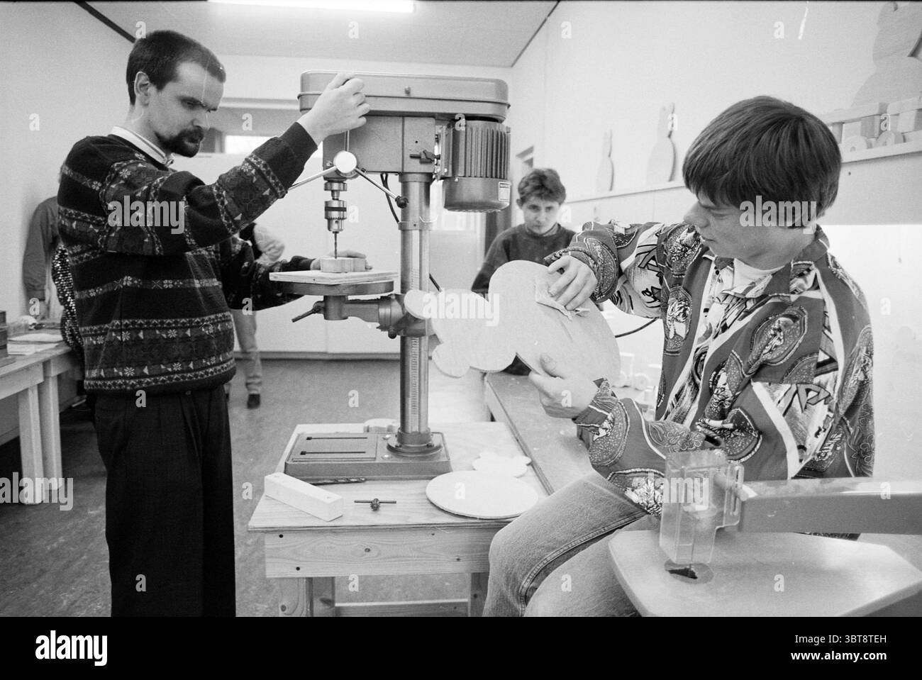 Attivita' 'Centro diurno' IJmuiden IJmuiden Paesi Bassi, Whizgle News, Dutch Desk, Paesi Bassi, 1950 - 2000 il 10-02-1994. L'immagine contiene questi argomenti. La scena si svolge in un laboratorio, pieno di un'aria di creatività e operosità. Due figure sono prominentemente impegnate nel lavoro artigianale. A sinistra, un uomo si trova davanti a una macchina di perforazione, concentrata e precisa. È vestito con pantaloni scuri e un pullover a motivi geometrici che aggiunge un tocco di carattere, in contrasto con l'ambiente utilitario. La sua espressione trasmette concentrazione e posiziona con attenzione un pezzo di legno sotto il trapano. Alla r Foto Stock