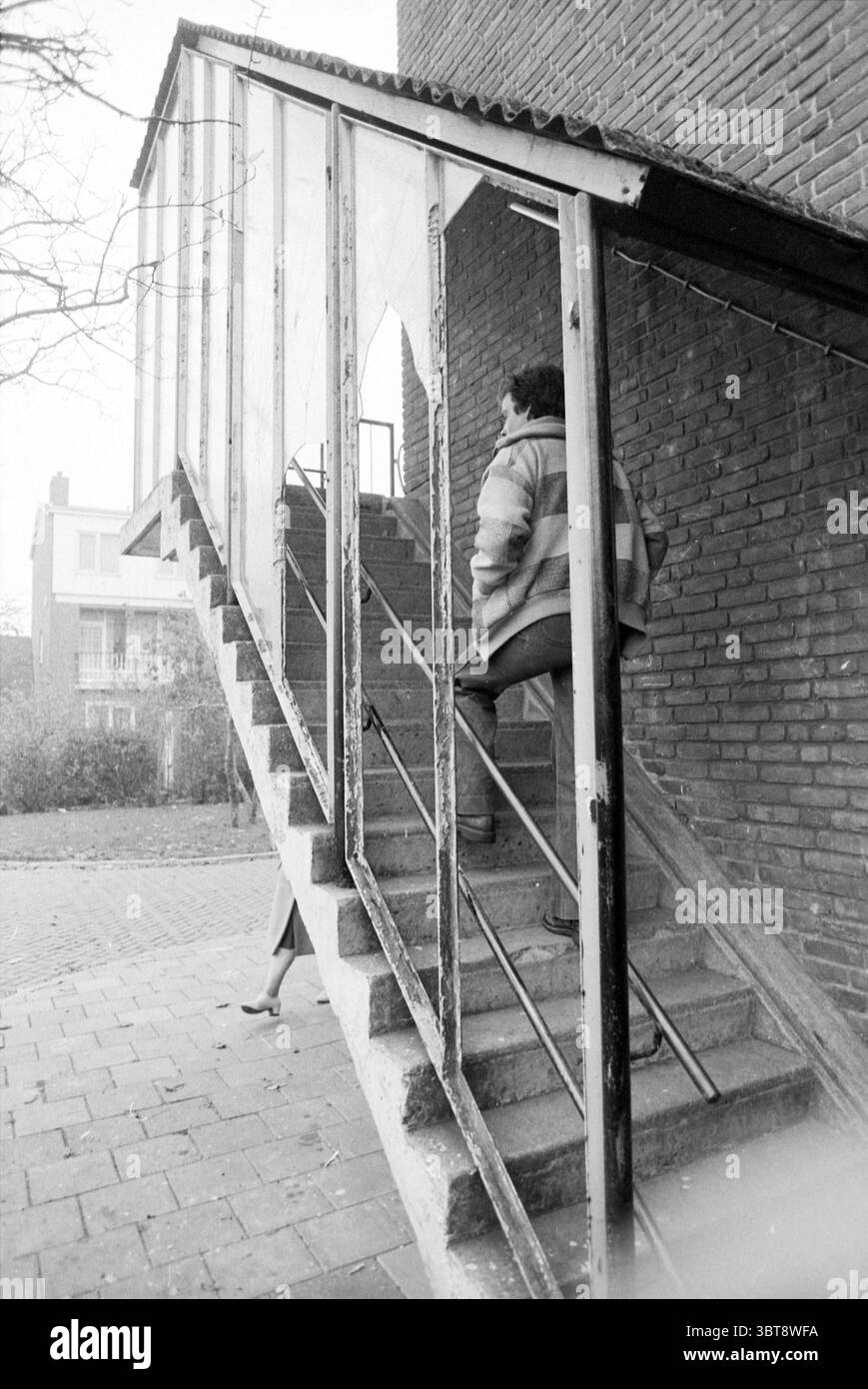 Bad Houses Hillegom Houses and House Construction, Whizgle News, Dutch Desk, Paesi Bassi, 1950 - 2000 il 07-11-1978. Questi argomenti sono mostrati nell'immagine. La scena presenta una scalinata di rilievo in cemento, che conduce da un livello inferiore. I gradini sono incorniciati da una struttura trasparente su un lato, creando una sensazione un po' chiusa. Si vede una persona salire la scala, parzialmente oscurata dai pannelli in vetro. Indossano una giacca leggera a righe, che suggerisce un comportamento casual ma premuroso mentre navigano sui gradini. Sullo sfondo, l'impostazione è caratterizzata da un mix di Foto Stock