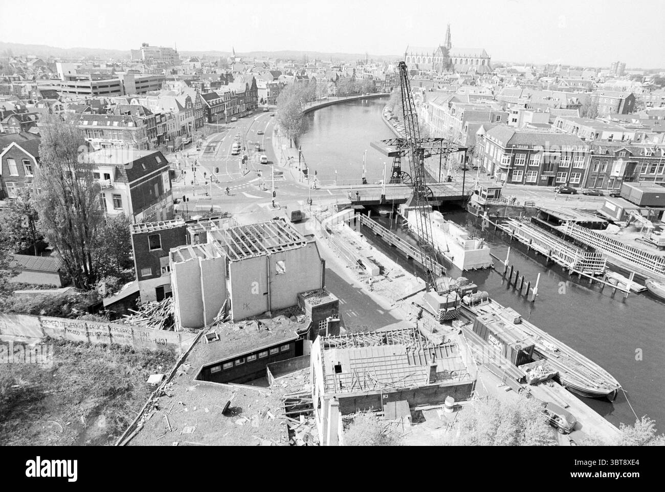 Edifici demoliti South Buiten Spaarne Haarlem Zuider Buiten Spaarne Paesi Bassi, Whizgle News, Dutch Desk, Paesi Bassi, 1950 - 2000 il 28-04-1994. L'immagine include questi argomenti. La scena offre un vasto paesaggio urbano, segnato dall'interazione tra architettura e corsi d'acqua. In primo piano, varie strutture sono in vari stati di costruzione o decostruzione, con impalcature visibili e materiali esposti che indicano uno sviluppo in corso. Diverse barche fiancheggiano il canale, i loro scafi che sporgono nell'acqua, aggiungendo un senso di dinamismo alla scena. Il canale stesso scorre Foto Stock