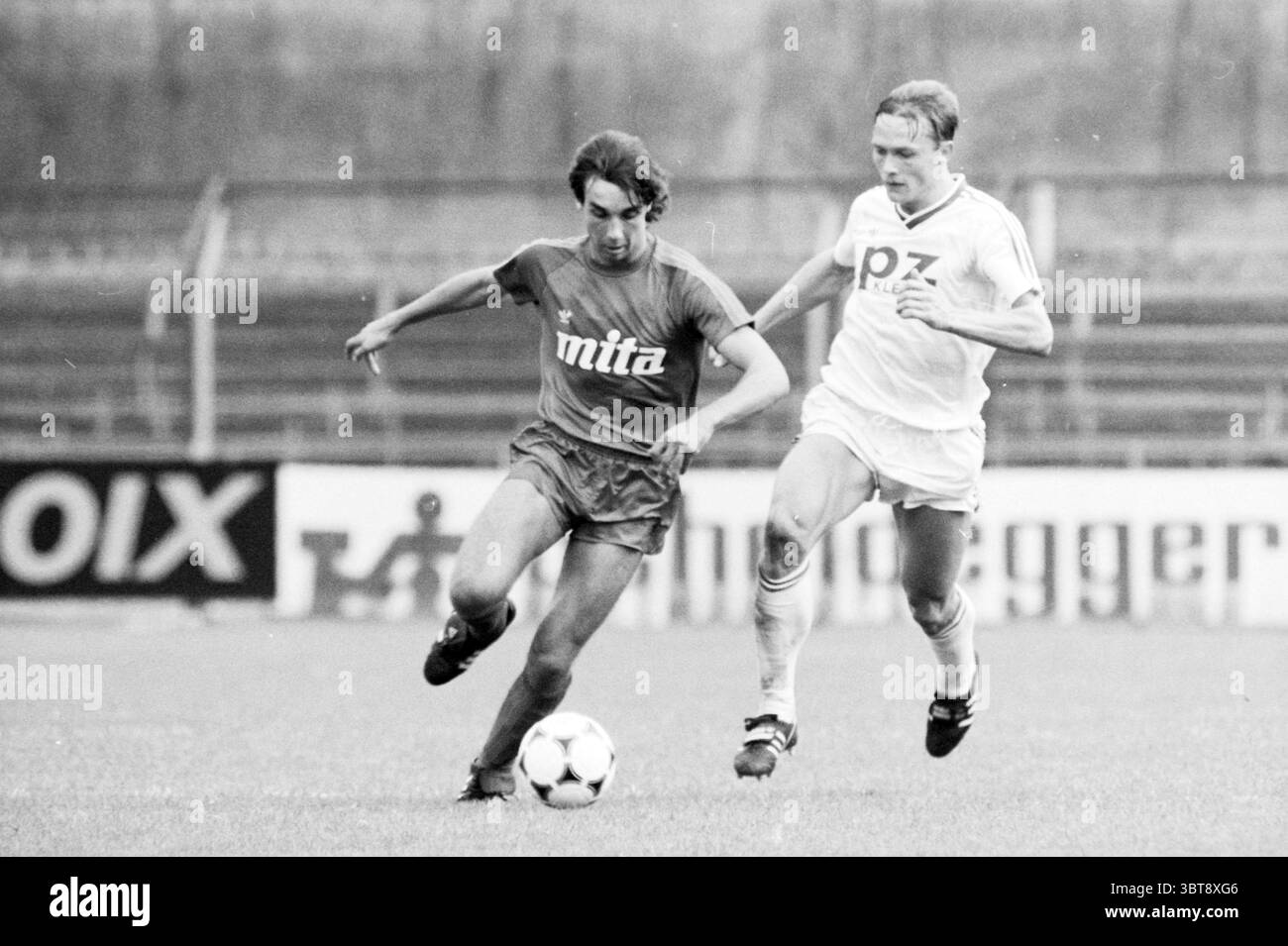 Haarlem Go Ahead Eagles Football Haarlem, Whizgle News, Dutch Desk, Paesi Bassi, 1950 - 2000 il 08-09-1985. L'immagine mostra questi argomenti. La scena cattura un momento intenso su un campo di calcio, dove due giocatori sono impegnati in un inseguimento vivace. A sinistra, un giocatore, vestito con una maglia rossa brillante con un design semplice e pantaloncini coordinati, sembra controllare sapientemente la palla con il piede. La sua postura è dinamica; una gamba si estende in avanti, mostrando agilità e concentrazione. La sua espressione è determinata, sottolineando la natura competitiva del gioco. Dietro, il secondo giocatore è c Foto Stock
