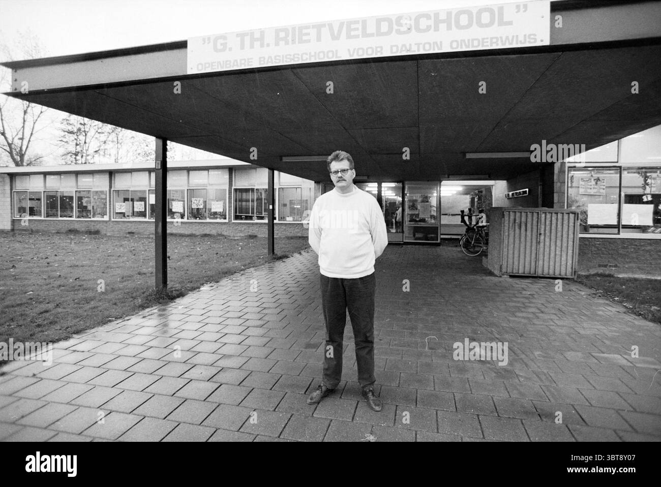 Sig. Wagenaar per la Scuola di Rietveld, Whizgle News, Dutch Desk, Paesi Bassi, 1950 - 2000 il 06-11-1991. Questi argomenti vengono visualizzati nell'immagine. La scena vede un uomo in primo piano, che trasuda un comportamento composto. È vestito con un maglione di colore chiaro e sembra essere nel suo periodo di mezzo, con occhiali che aggiungono un tocco accademico. La sua espressione è neutrale, suggerendo una calma. Lo sfondo rivela una moderna struttura architettonica caratterizzata da tetti piatti e grandi finestre. Questo edificio trasmette un senso di scopo istituzionale, probabilmente fungendo da fa educativo Foto Stock