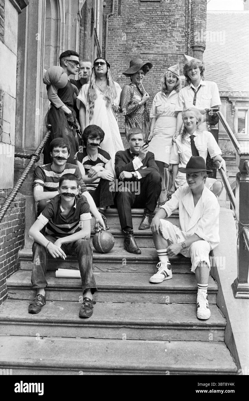 Gruppo di giovani vestiti da personaggi famosi gruppi abbigliamento, Whizgle News, Dutch Desk, Paesi Bassi, 1950 - 2000 il 06-08-1983. L'immagine contiene questi argomenti. La scena cattura un gruppo vivace disposto su una serie di ampi gradini di pietra che conducono ad un grande edificio. La facciata della struttura è caratterizzata da classici mattoni, che si aggiungono all'atmosfera storica. In cima ai gradini sono riuniti diversi individui, tutti vestiti con una serie di abiti che sembrano riflettere un incontro giocoso o a tema. Alcuni indossano cappelli e occhiali da sole, suggerendo un'atmosfera festosa. Le loro posture sono rilassate a. Foto Stock