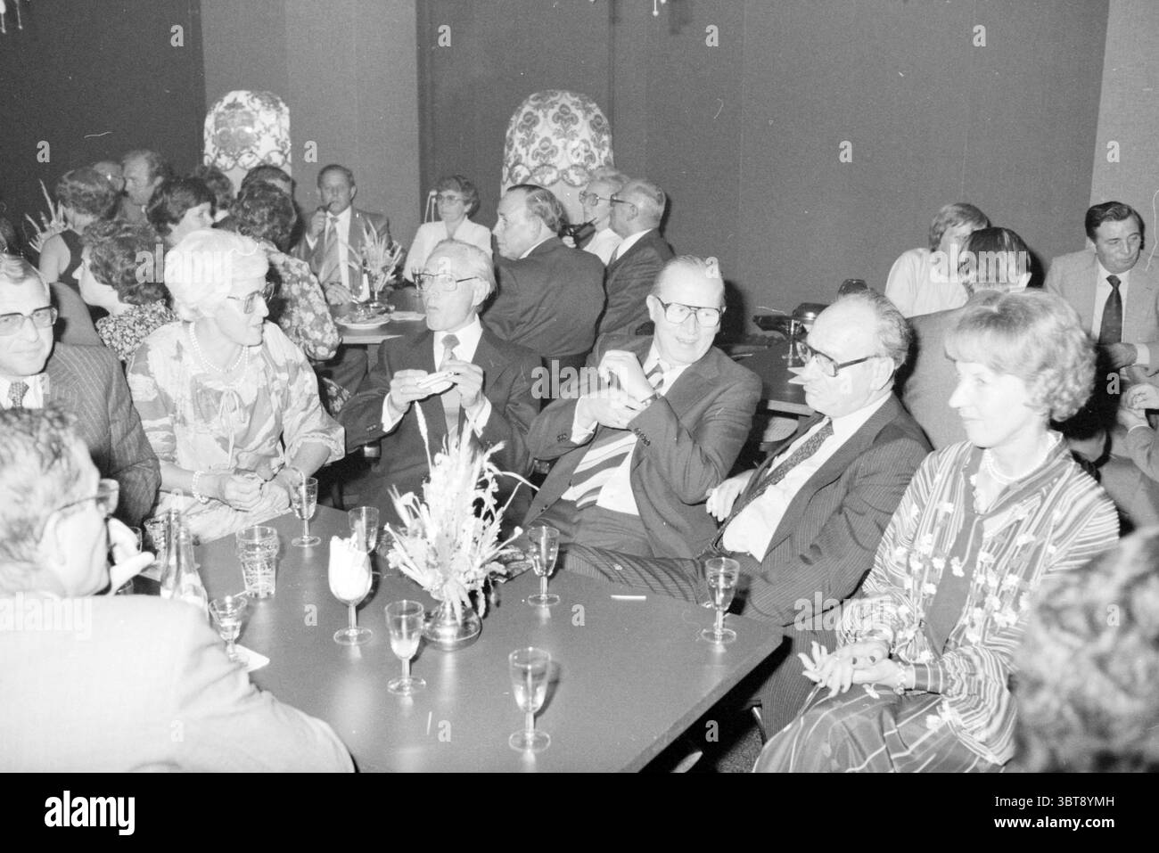 Anniversario Sig. A Bokhorst Equipment Department Spaarndam Stevin Group, Whizgle News, Dutch Desk, Paesi Bassi, 1950 - 2000 on 29-09-1978. L'immagine include questi argomenti. La scena cattura un incontro di diverse persone sedute intorno a un tavolo oscuro, creando un'atmosfera di conversazione e coinvolgimento sociale. L'ambiente sembra essere uno spazio formale o semi-formale, probabilmente una sala banchetti o un'area riservata in un ristorante, caratterizzato da un'illuminazione silenziosa che aggiunge un'atmosfera intima. I partecipanti, un mix di uomini e donne di varie età, sono vestiti con una gamma di abbigliamento formale. Alcuni W Foto Stock