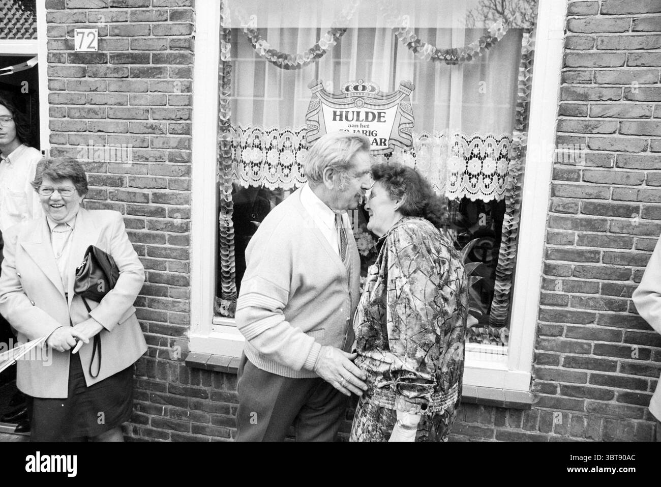 50 anni Kleijen@orst, Whizgle News, Dutch Desk, Paesi Bassi, 1950 - 2000 il 24-03-1992. Questi sono gli elementi dell'immagine. In un ambiente urbano vivace, una coppia si trova in prima linea, impegnata in un momento intimo, condividendo un bacio gioioso. L'uomo, vestito con un cardigan di colore chiaro e pantaloni scuri, ha una calda espressione, mentre la donna accanto a lui, con un vestito colorato e fantasia, irradia con gioia. C'è un'energia giocosa nella loro interazione, che suggerisce una festa o un'occasione speciale. Dietro di loro, un gruppo di spettatori aumenta la vivacità della scena. A sinistra, una donna Foto Stock