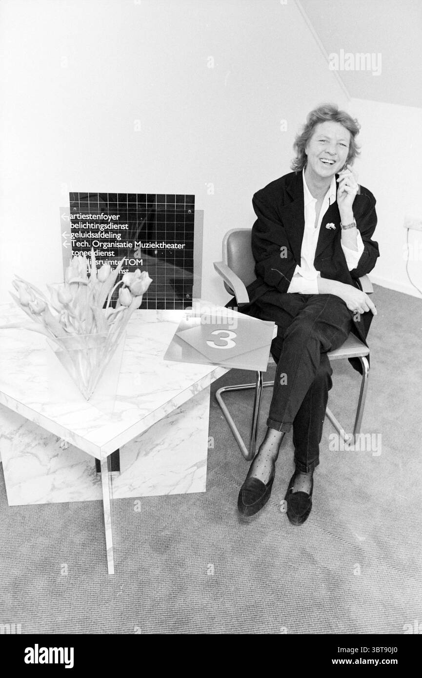 Josephine Dam designer Bloemendaal Clothing Bloemendaal, Whizgle News, Dutch Desk, Paesi Bassi, 1950 - 2000 il 03-02-1988. L'immagine contiene questi argomenti. In un ambiente moderno e minimalista, una persona siede comodamente su una sedia metallica elegante. Sono vestiti con un elegante blazer nero, che trasuda un senso di professionalità ed eleganza casual. La scena è incentrata su un piccolo tavolo con ripiano in marmo bianco che presenta un motivo sottile e organico che aggiunge un tocco di raffinatezza. Sul tavolo, un bouquet di fiori freschi in delicate sfumature di rosa e bianco donano un elemento di calore e di vita a questo Foto Stock