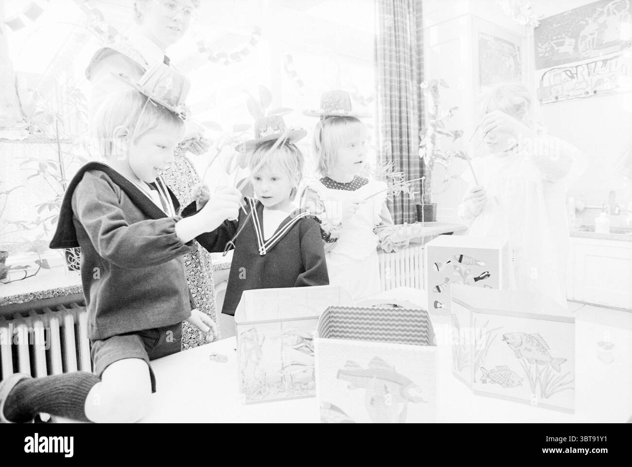 Prescolare Play Day in occasione di 50 anni di Noorder Kindergarten asilo asilo nido, Whizgle News, Dutch Desk, Paesi Bassi, 1950 - 2000 il 01-11-1979. L'immagine mostra questi argomenti. In un ambiente interno luminoso e vivace, un piccolo gruppo di bambini è impegnato in un'attività creativa. Lo spazio è pieno di luce soffusa e diffusa, che illumina la scena con un'atmosfera allegra. Quattro bambini sono in prima linea nella composizione. Un bambino, vestito con un abito scuro con un colletto a vela, è profondamente concentrato su un compito delicato, magari realizzando o assemblando qualcosa con la sua ha Foto Stock