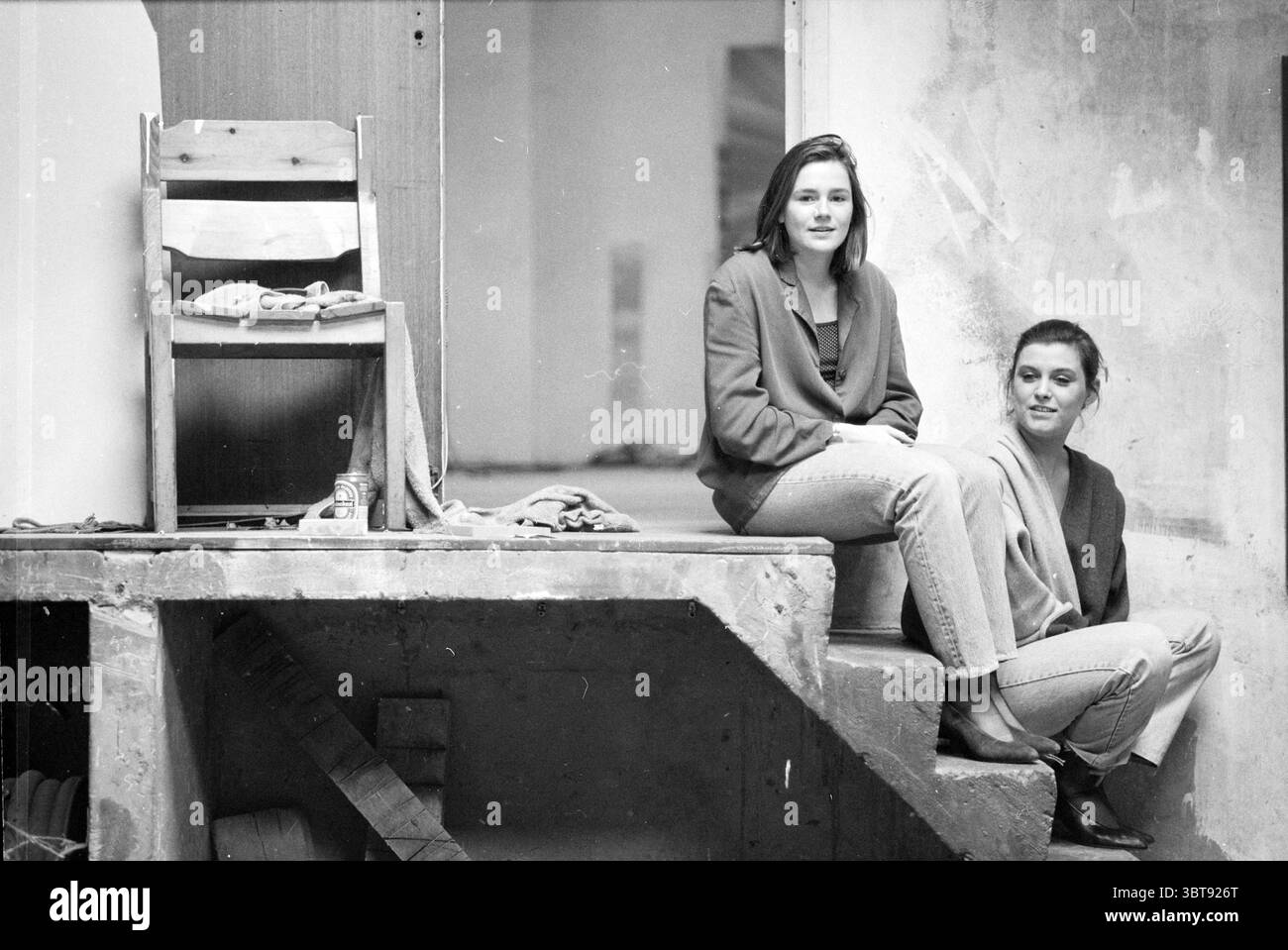 Ladies Muller and Hagemans impressario, Whizgle News, Dutch Desk, Paesi Bassi, 1950 - 2000 il 30-03-1992. L'immagine include questi argomenti. La scena presenta due donne sedute su una scala in cemento. L'ambiente sembra essere un interno minimalista, possibilmente uno studio d'arte o una galleria, caratterizzato dai suoi elementi architettonici grezzi. Le pareti sono incompiute, rivelando accenni di texture e colore che evocano un senso di semplicità rustica. Le donne trasudano un comportamento rilassato ma contemplativo. Una si siede casualmente con le gambe incrociate, indossando un cardigan drappeggiato sulle spalle. L'altro Foto Stock