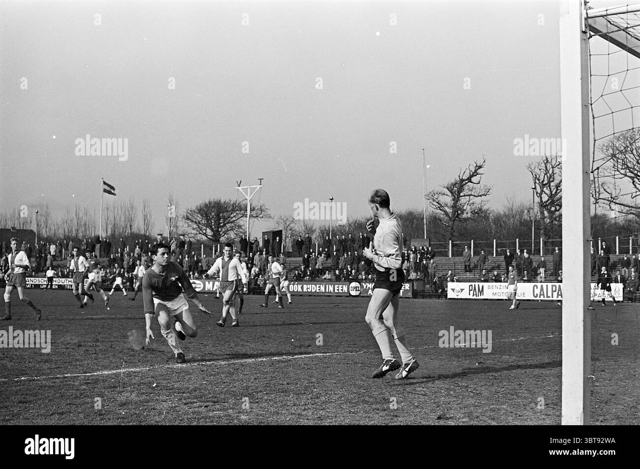 Stormvogels - Hoofddorpse Boys Football, Whizgle News, Dutch Desk, Paesi Bassi, 1950 - 2000 il 11-04-1964. Questi sono gli argomenti nell'immagine. In una scena dinamica su un campo da calcio, l'atmosfera è carica di energia e anticipazione. L'ambientazione presenta un campo erboso ben mantenuto che contrasta con il cielo scuro e coperto, suggerendo un imminente cambiamento del tempo. A margine, si è riunita una grande folla, le loro figure sono sfocate e indistinte, creando un senso di eccitazione collettiva. Da un lato della scena, i giocatori partecipano al gioco. Un portiere, vestito con un distinto Foto Stock