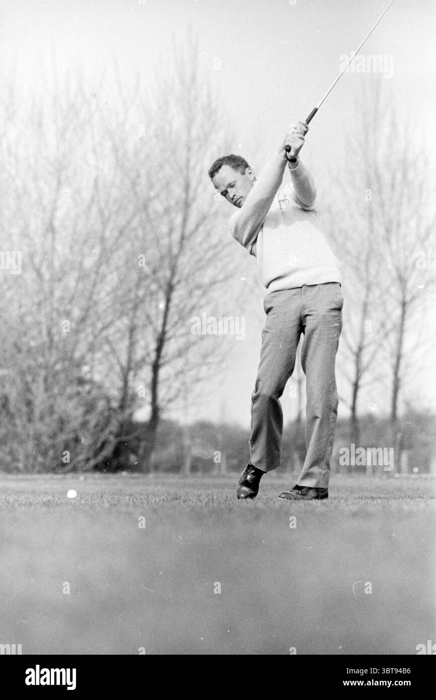 Golfclub Spaarnwoude Golf Golf Spaarnwoude, Whizgle News, Dutch Desk, Paesi Bassi, 1950 - 2000 il 02-05-1983. Questi sono gli argomenti nell'immagine. In questa scena, un uomo è in posizione intermedia mentre pratica la sua tecnica di golf. Mostra un'espressione focalizzata, incarnando concentrazione e determinazione. Il suo abbigliamento è composto da un maglione di colore chiaro sovrapposto a una camicia con colletto, abbinato a pantaloni a righe pressati con cura che donano un tocco di raffinatezza all'ambientazione. Il golf club si estende indietro, sottolineando il movimento fluido e la tensione del momento. La sua postura è atletica, W Foto Stock