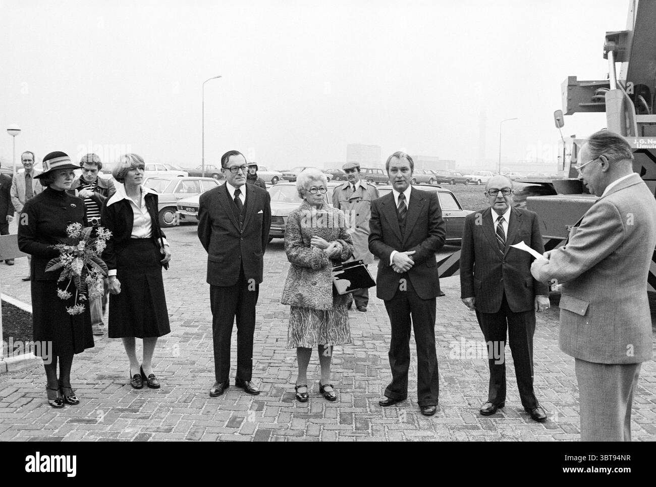 Opening J.G. Nelis Waardepolder J.G. Nelis IJmuiden Opening Openings commissioning, Whizgle News, Dutch Desk, Paesi Bassi, 1950 - 2000 on 30-10-1976. Questi argomenti sono mostrati nell'immagine. In un ambiente silenzioso caratterizzato da un'atmosfera nebbiosa e ricoperta di nuvole, un gruppo di individui ben vestiti si erge in modo prominente su una superficie acciottolata. La scena è ambientata su uno sfondo con veicoli parcheggiati in disordine, che accennano a un raduno pubblico o ufficiale. I colori dell'ambiente sono soffocati, dominati da grigi e neri, che contribuiscono a creare un'atmosfera seria e formale. Tra le persone presenti, Foto Stock