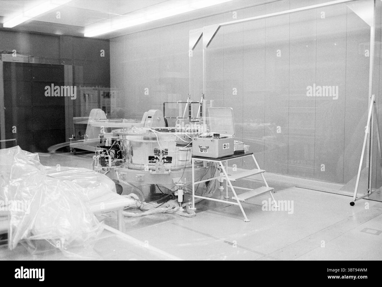 Installazione tecnica presso Fokker Ruimtevaart, Whizgle News, Dutch Desk, Paesi Bassi, 1950 - 2000 il 04-12-1980. Questi argomenti vengono visualizzati nell'immagine. La scena presenta un ambiente sterile e clinico, caratterizzato da una predominanza di toni bianchi e grigi. Il pavimento è una superficie liscia che riflette l'illuminazione superiore, che emette un bagliore fresco e luminoso, migliorando la pulizia dello spazio. Al centro si trova un grande apparato circolare composto da elementi metallici e vetro trasparente. Questo dispositivo dispone di più collegamenti e tubi che si estendono da esso, suggerendo una funzione complessa, po Foto Stock Installazione tecnica presso Fokker Ruimtevaart, Whizgle News, Dutch Desk, Paesi Bassi, 1950 - 2000 il 04-12-1980. Questi argomenti vengono visualizzati nell'immagine. La scena presenta un ambiente sterile e clinico, caratterizzato da una predominanza di toni bianchi e grigi. Il pavimento è una superficie liscia che riflette l'illuminazione superiore, che emette un bagliore fresco e luminoso, migliorando la pulizia dello spazio. Al centro si trova un grande apparato circolare composto da elementi metallici e vetro trasparente. Questo dispositivo dispone di più collegamenti e tubi che si estendono da esso, suggerendo una funzione complessa, po Foto Stock