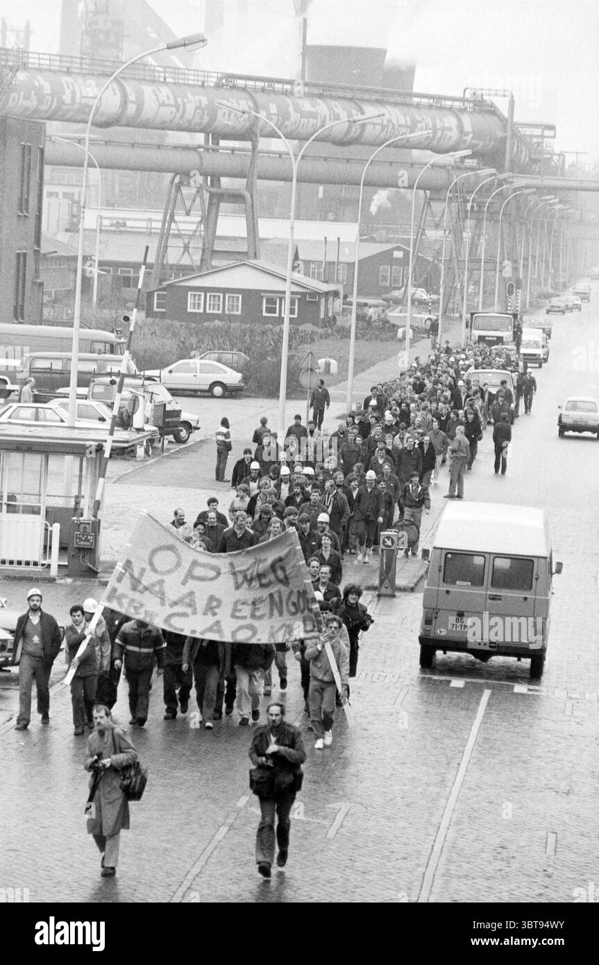 Dimostrazione negoziati collettivi sul contratto di lavoro Blast Furnaces dimostrazione Blast Furnaces, Whizgle News, Dutch Desk, Paesi Bassi, 1950 - 2000 il 05-04-1985. Questi argomenti vengono visualizzati nell'immagine. Un grande gruppo di individui marcia lungo un'ampia strada, creando un movimento potente e unificato. I partecipanti, vestiti con una gamma di abbigliamento casual, mostrano un mix di colori scuri e cappotti a motivi geometrici, riflettendo un approccio più cupo e utilitario all'abbigliamento. Alcuni indossano cappelli e sciarpe, a indicare il clima fresco. In primo piano, una bandiera prominente viene tenuta in alto, anche se io Foto Stock
