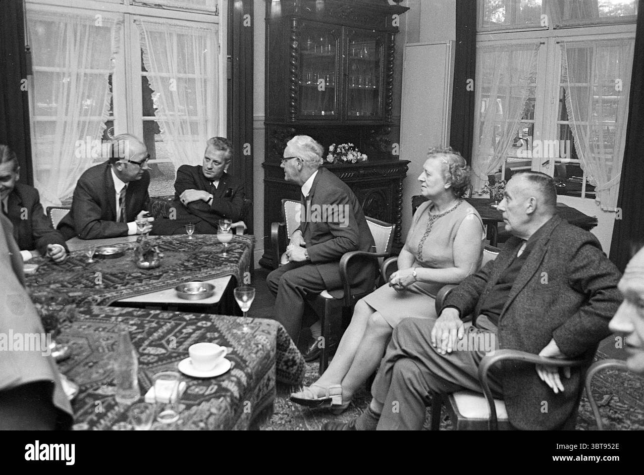 Cerimonia di premiazione TramvogelTournament Noord Zuid Hollandse Vervoersmaatschappij N.V. NZ, Whizgle News, Dutch Desk, Paesi Bassi, 1950 - 2000 il 17-09-1970. L'immagine mostra questi argomenti. In un interno illuminato con calore, un gruppo di sei persone si impegna a conversare intorno a un tavolo riccamente decorato. L'ambiente sembra trasudare un'aria di intimità e cameratismo. Le pareti sono adornate con pannelli di legno scuro, che completano i mobili ornati sullo sfondo, tra cui un grande armadietto con vetreria e oggetti decorativi. Le persone sono sedute in un semicerchio, con espressioni che vanno da Foto Stock