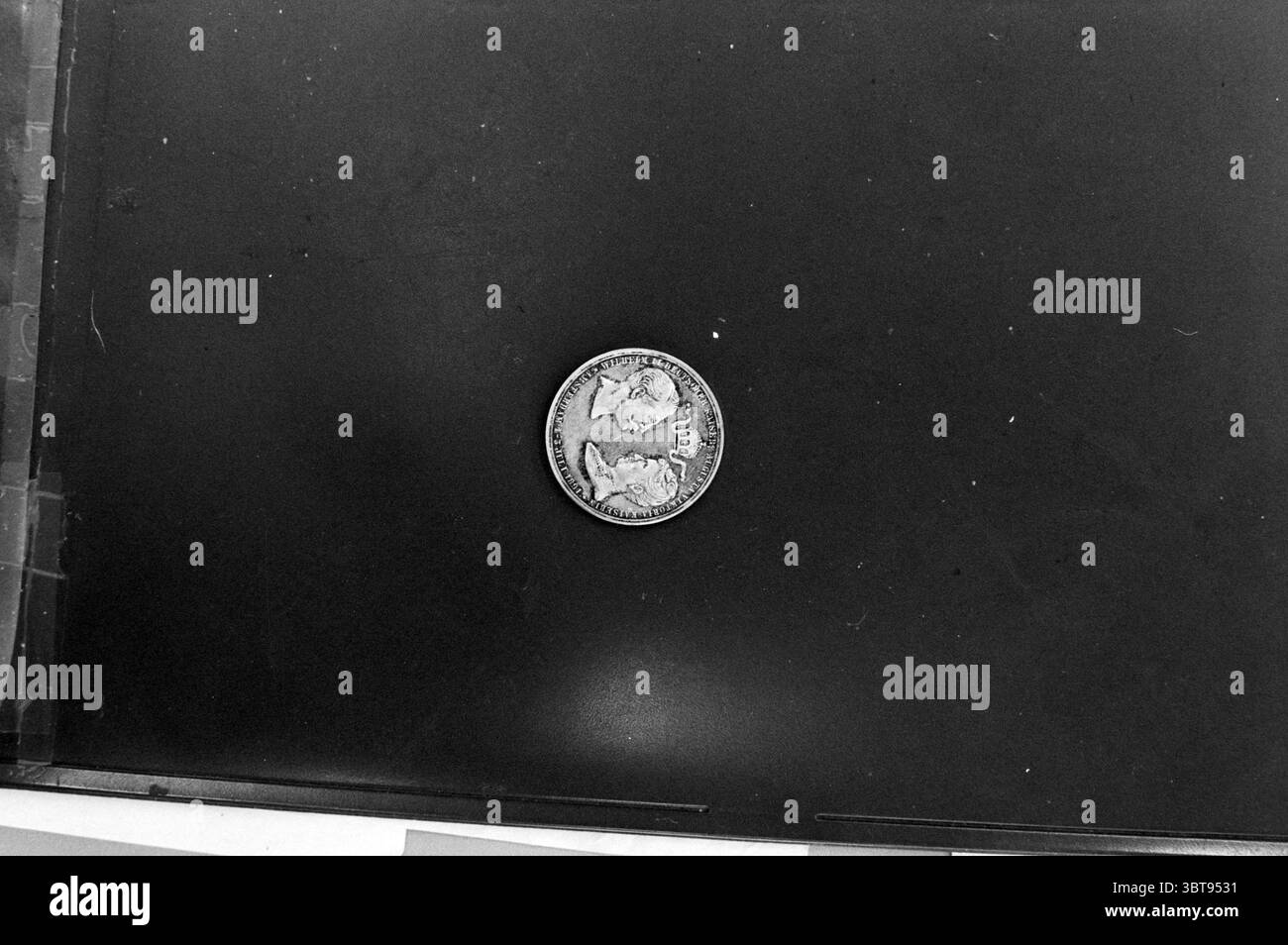 Moneta commemorativa in occasione della visita della coppia imperiale tedesca nei Paesi Bassi 1 - 3 luglio 1891., Whizgle News, Dutch Desk, Paesi Bassi, 1950 - 2000. L'immagine contiene questi argomenti. La scena visiva presenta una singola moneta posizionata centralmente su una superficie liscia e scura. La moneta, rotonda e metallica, mostra una patina d'epoca con disegni intricati sulla parte anteriore e posteriore. I dettagli mostrano figure e simboli che suggeriscono un significato storico, ma il contesto delle immagini rimane poco chiaro. La superficie sottostante è prevalentemente nera, il che migliora il contrasto e disegna un Foto Stock