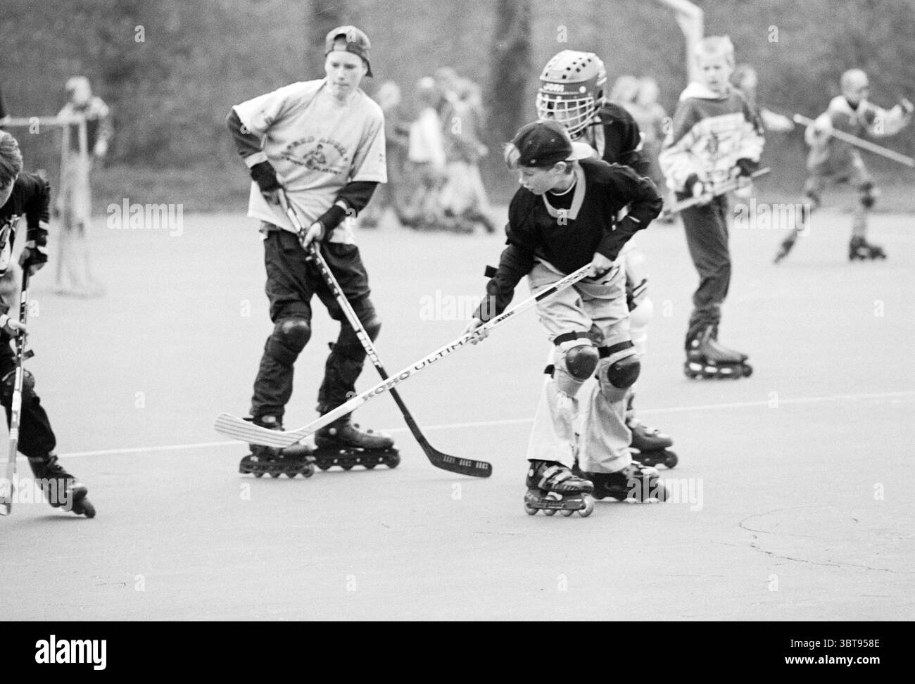 Hockey di strada Velsen-Zuid Velsen-Zuid, Whizgle News, Dutch Desk, Paesi Bassi, 1950 - 2000 il 21-04-1995. Questi sono gli elementi dell'immagine. In un ambiente aperto all'aperto, un gruppo di bambini è impegnato in una partita di hockey a rotelle su una superficie liscia e asfaltata. La scena è piena di energia e movimento, mentre i giocatori pattinano rapidamente, i loro corpi si inclinano in avanti con determinazione mirata. I bambini indossano un mix di stili di abbigliamento, mostrando una gamma di colori. Alcune t-shirt sportive con vestibilità morbida, mentre altre hanno maniche lunghe, che creano un contrasto con la palette morbida del contorno Foto Stock
