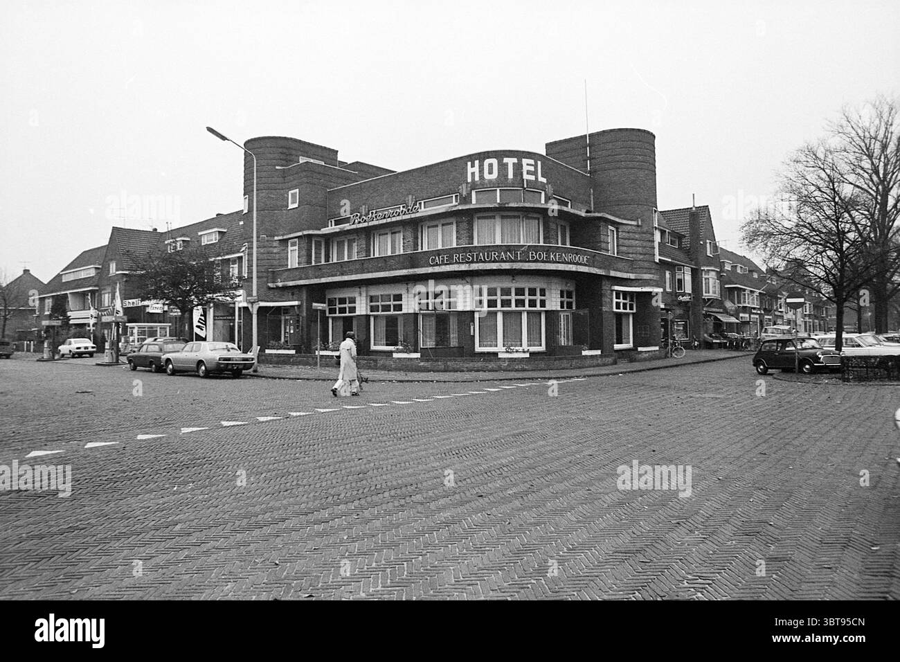 Bar ristorante dell'hotel Boekenroode Heemstede Zandvoortselaan Paesi Bassi., Whizgle News, Dutch Desk, Paesi Bassi, 1950 - 2000. Questi sono gli argomenti nell'immagine. La scena e' caratterizzata da un edificio in mattoni ben segnalato come un hotel, caratterizzato dal suo stile architettonico distintivo. L'esterno è delineato da una facciata di mattoni rossi, che conferisce un aspetto classico e robusto. Sopra l'ingresso, grandi finestre invitano a scorci dell'interno, mentre il piano terra presenta un'accogliente entrata con baldacchino. In primo piano, una persona vestita con abiti di colore chiaro viene vista attraversare un co Foto Stock
