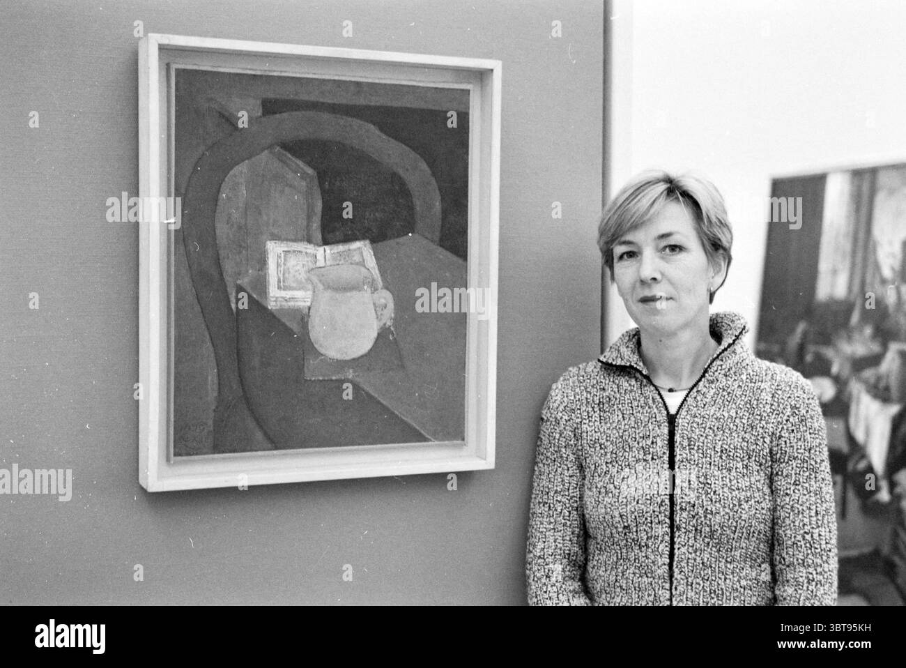 Tre dipendenti del Frans Hals Museum e Verweyhal Haarlem Grote Markt Paesi Bassi, Whizgle News, Dutch Desk, Paesi Bassi, 1950 - 2000 il 05-12-1999. L'immagine include questi argomenti. In uno spazio interno minimalista, una donna si erge accanto a un'opera d'arte incorniciata esposta su una parete. Ha capelli corti e chiari e indossa un maglione grigio testurizzato che aggiunge un tocco di comfort alla scena. L'espressione sul suo volto appare contemplativa, suggerendo che potrebbe essere impegnata a pensare all'opera d'arte. L'opera d'arte stessa è una rappresentazione astratta, principalmente caratterizzata da toni tenui di marrone e beige Foto Stock