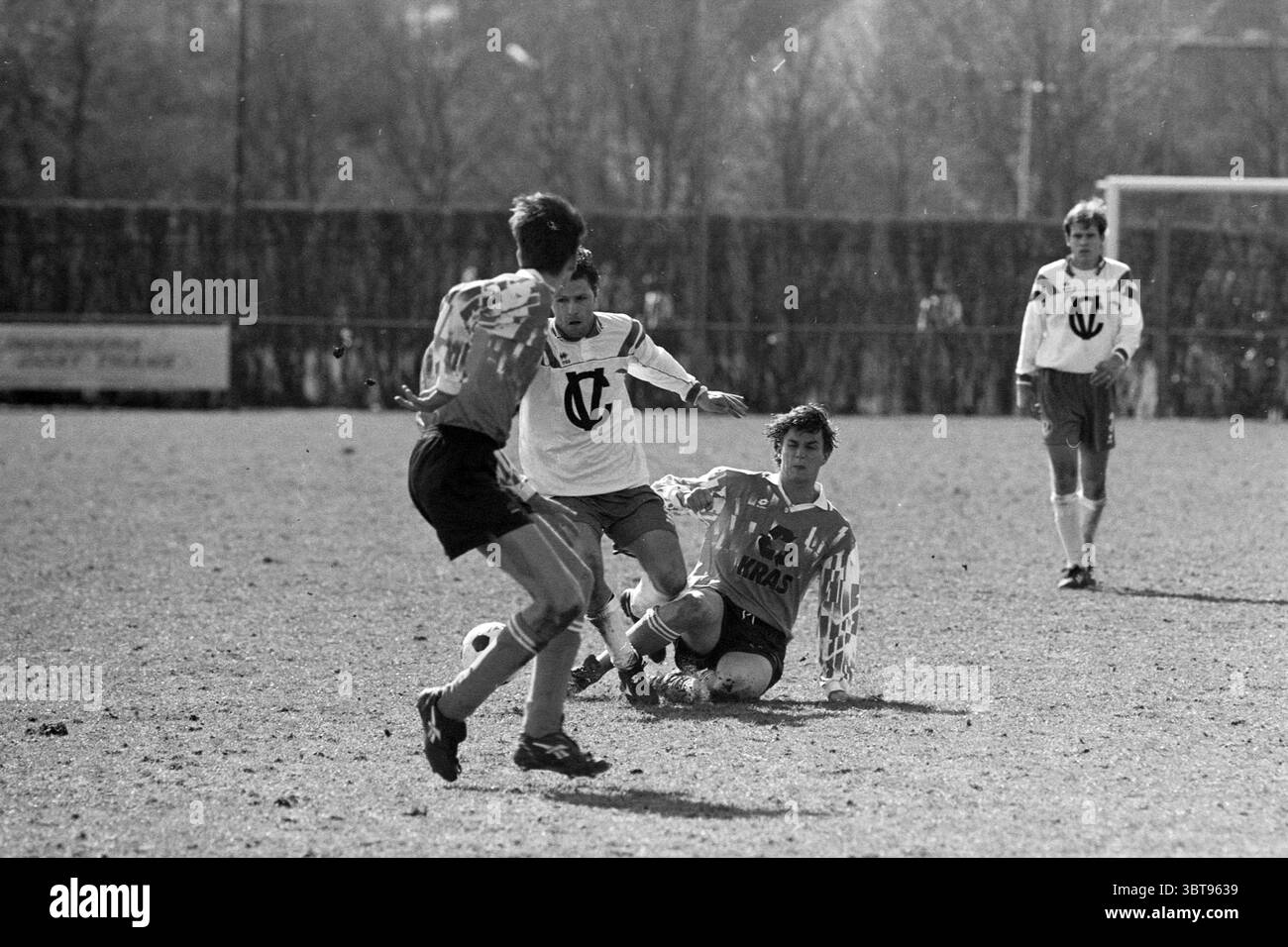 Football Fulmars - Volendam, Whizgle News, Dutch Desk, Paesi Bassi, 1950 - 2000 il 30-03-1996. L'immagine include questi argomenti. La scena cattura un momento dinamico su un campo da calcio erboso, situato in un'area aperta ben tenuta circondata da alti alberi indistinti che creano uno sfondo sfocato. L'azione è incentrata su tre giocatori impegnati in un gioco competitivo. Un giocatore che indossa una maglia bianca contrassegnata da un distintivo emblema è in primo piano, guidando abilmente la palla mentre scivola sull'erba. La sua espressione riflette determinazione e concentrazione. Un altro giocatore, rivestito con una o Foto Stock