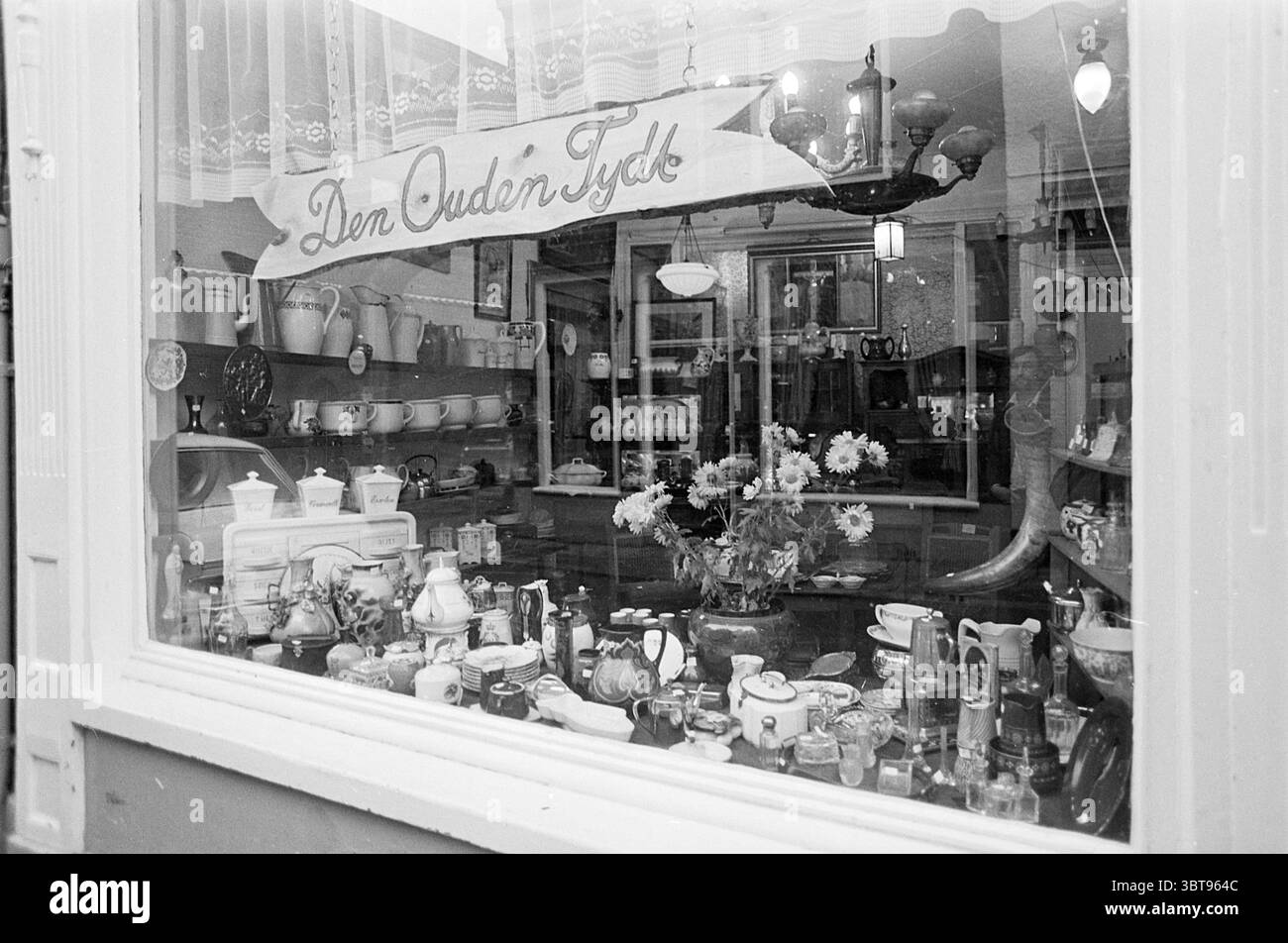 Negozi spazzatura 'Den Ouden Tijd' e 'Black Magic' uno accanto all'altro nei negozi e chioschi Kleine Houtstraat Haarlem Kleine Houtstraat Paesi Bassi, Whizgle News, Dutch Desk, Paesi Bassi, 1950 - 2000 su 11-12-1974. Questi sono gli argomenti nell'immagine. La scena affascina con una pittoresca esposizione di vari oggetti all'interno di una vetrina. Un'ampia gamma di utensili da cucina, tra cui teiere in porcellana, tazze delicate e barattoli di vetro scintillanti, è disposta con cura sugli scaffali, fornendo un senso di caos organizzato. Alcuni degli oggetti sono adornati con motivi intricati, che mostrano un mix di vibranti e mu Foto Stock