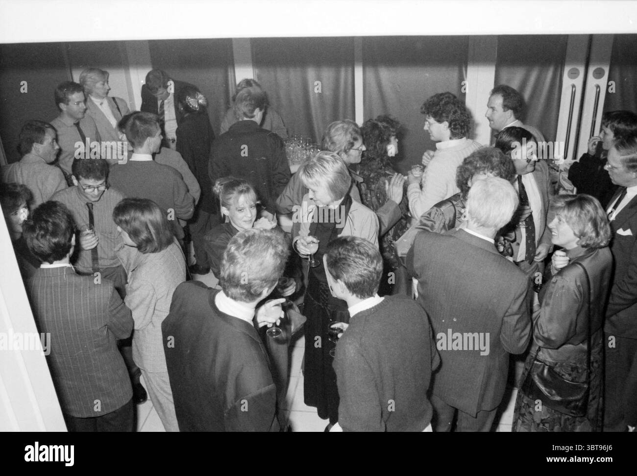 Serata di festa in tribunale a causa dell'apertura apertura inaugurazione Corte, Whizgle News, Dutch Desk, Paesi Bassi, 1950 - 2000 il 21-10-1987. Questi sono gli argomenti nell'immagine. La scena è animata da un raduno di persone, impegnate nella conversazione e nell'interazione sociale. Presenta un gruppo eterogeneo, alcuni vestiti con un abbigliamento formale, mentre altri appaiono più casual. L'abbigliamento include abiti, blazer e abiti, principalmente in colori tenui come grigio, nero e navy, con occasionali tonalità più chiare. L'ambiente è probabilmente un luogo interno con un'estetica moderna, caratterizzato da linee eleganti e un mini Foto Stock