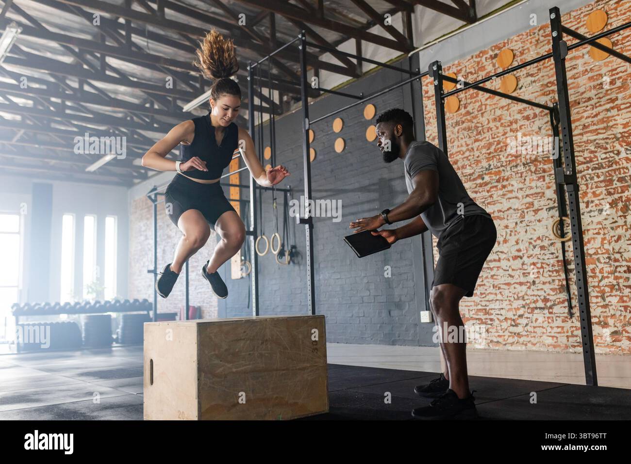 Diversi formatori e apprendisti che eseguono salti plyometrici in palestra con tablet e spazio per copiare Foto Stock