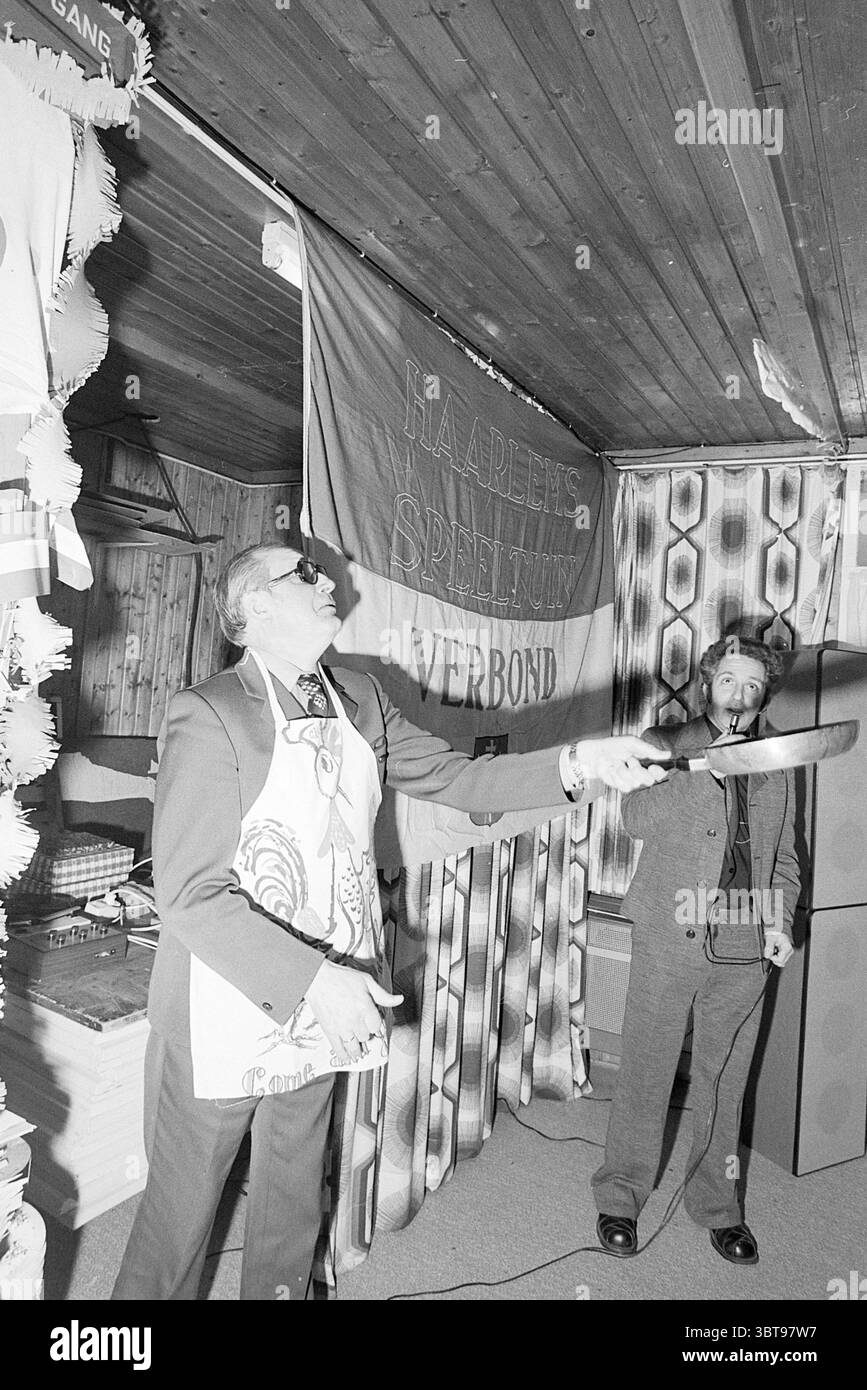 Pancake da forno presso il parco giochi associazione V.S.O.D. Playgrounds and Playgrounds, Whizgle News, Dutch Desk, Paesi Bassi, 1950 - 2000 il 15-01-1977. L'immagine mostra questi argomenti. In una vivace scena interna, un gruppo di persone si impegna in un'atmosfera festosa, evidenziata da decorazioni che adornano le pareti e il soffitto in legno. L'atmosfera riflette un senso di celebrazione, impreziosito da striscioni colorati e drappi in tessuto che creano uno sfondo vivace. Un individuo, posizionato centralmente e con indosso una tuta ricoperta da grembiule, tiene un grande cucchiaio in alto come se guidasse un'azione cerimoniale. Il suo ex Foto Stock