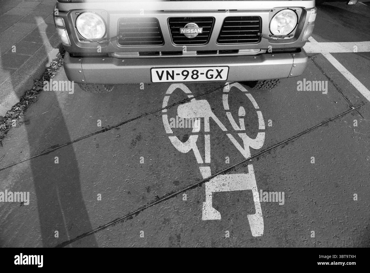 Area di pre-smistamento biciclette Hillegom, Whizgle News, Dutch Desk, Paesi Bassi, 1950 - 2000 on 28-10-1991. L'immagine include questi argomenti. La scena presenta un veicolo parcheggiato sopra un'area designata per le biciclette. Il veicolo, che ha un aspetto robusto e robusto, è verniciato in un colore neutro, possibilmente grigio o argento. La griglia anteriore è in primo piano, evidenziando il marchio del veicolo. Il terreno sotto il veicolo è contrassegnato da un'icona bianca che simboleggia una bicicletta, indicando chiaramente le limitazioni per il parcheggio. Questo simbolo si distingue contro la superficie più scura del marciapiede Foto Stock