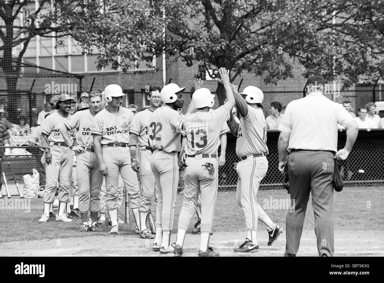 Baseball Kinheim - Pirati, Whizgle News, Dutch Desk, Paesi Bassi, 1950 - 2000 il 07-06-1992. Questi argomenti sono mostrati nell'immagine. La scena raffigura una vivace partita di baseball in un campo erboso, con giocatori in uniformi vivaci che celebrano un gioco. I membri del team indossano camicie abbinate nelle tonalità blu chiaro e arancione, con una numerazione affilata sulla schiena. In primo piano, un piccolo gruppo di quattro giocatori si batte entusiasticamente a vicenda, le loro espressioni riflettono gioia e cameratismo, suggerendo di aver appena segnato o ottenuto qualcosa di significativo durante la partita. swa a un giocatore Foto Stock