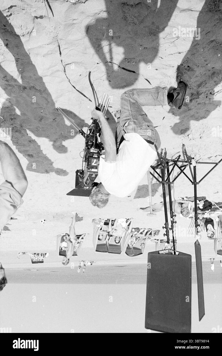 Registrazione di film mini e maxi a Zandvoort riprese di registrazioni cinematografiche Zandvoort, Whizgle News, Dutch Desk, Paesi Bassi, 1950 - 2000 il 08-09-1988. L'immagine mostra questi argomenti. La scena raffigura un vivace ambiente da spiaggia in una giornata di sole, caratterizzato da una distesa sabbiosa che si estende verso l'oceano. In primo piano, un uomo è posizionato con una videocamera montata su un treppiede, che appare concentrato e impegnato nel suo compito. Indossa una camicia di colore chiaro e jeans casual, che si fondono con l'atmosfera rilassata tipica di un ambiente da spiaggia. Le ombre degli oggetti vicini si estendono delicatamente attraverso la san Foto Stock