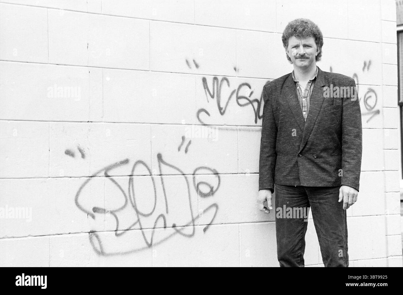 Cantante Rob Moeke Lakenstraat 33 cantante e cori Haarlem Lakenstraat Paesi Bassi, Whizgle News, Dutch Desk, Paesi Bassi, 1950 - 2000 il 26-04-1988. Questi argomenti sono mostrati nell'immagine. In un ambiente urbano informale, un uomo si erge contro una parete dai colori chiari e testurizzati che presenta graffiti artistici. I graffiti, realizzati in vernice spray scura, aggiungono un elemento di cultura urbana alla scena. L'abbigliamento da uomo è composto da un blazer aderente su una camicia a quadri, abbinato a jeans scuri, che gli conferiscono un aspetto rilassato ma leggermente formale. I suoi capelli sono ricci e curati, e lui ha una focu Foto Stock