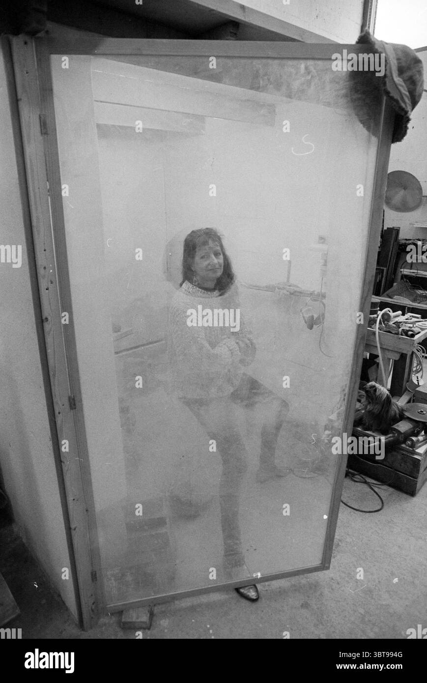 Lia Versteege artista, Whizgle News, Dutch Desk, Paesi Bassi, 1950 - 2000 on 27-10-1993. L'immagine contiene questi argomenti. La scena raffigura una figura seduta all'interno di un involucro traslucido, creando un senso di intrigo e isolamento. La persona è vestita con un comodo maglione dai colori chiari abbinato a pantaloni scuri, la sua postura rilassata ma contemplativa. Il contenitore ha una qualità simile a quella del vetro, leggermente appannato o oscurato, che aggiunge un'atmosfera onirica ed eterea alla composizione. Intorno alla figura, l'ambientazione sembra essere un laboratorio o uno studio, con vari strumenti e oggetti sparsi, Foto Stock