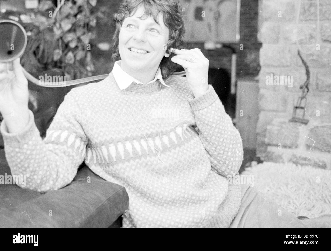 Onorevole Roorda Heemstede Persons Heemstede Paesi Bassi, Whizgle News, Dutch Desk, Paesi Bassi, 1950 - 2000 il 14-04-1983. Questi sono gli elementi dell'immagine. La scena cattura un ambiente interno accogliente, caratterizzato da toni caldi e silenziosi. Una persona si siede comodamente su un divano in pelle scura, vestito da un maglione di colore chiaro con un caratteristico motivo testurizzato che mostra un design giocoso nelle tonalità del bianco e del grigio. Hanno capelli corti e leggermente ondulati e un sorriso luminoso, che suggeriscono un umore leggero. Nella mano destra, trattengono un oggetto flessibile che sembra essere un tubo o una cinghia, s Foto Stock