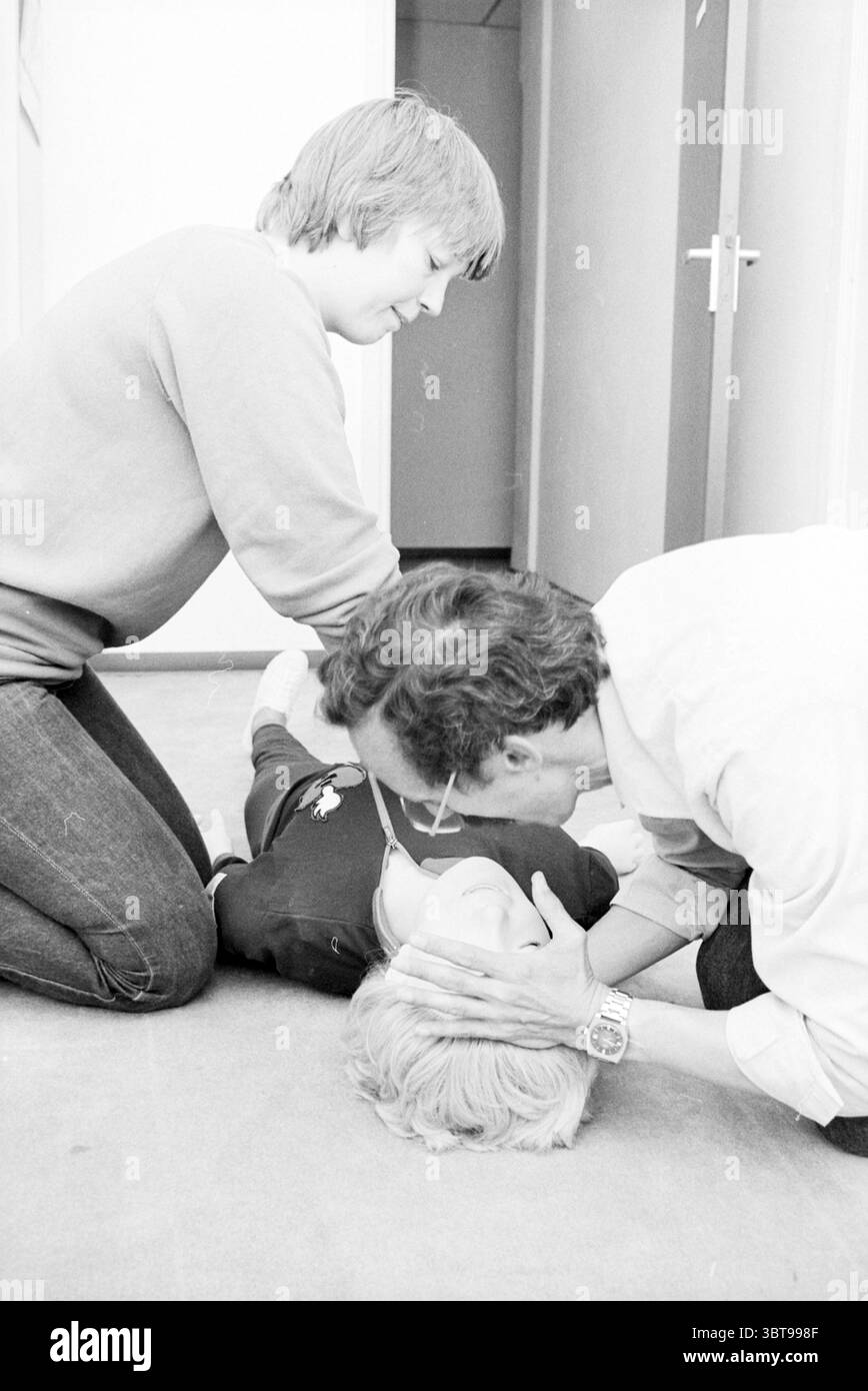 Uomo e donna dimostrano massaggio al petto con manichino durante Cross union, Whizgle News, Dutch Desk, Paesi Bassi, 1950 - 2000 il 30-09-1980. Questi sono gli argomenti nell'immagine. In uno spazio interno ben illuminato, sono presenti tre persone, impegnate in una scena tesa e urgente. Il pavimento è ricoperto da un tappeto dai toni neutri, contribuendo alla serietà dell'atmosfera. Due personaggi si inginocchiano a terra. Una, una persona con capelli marrone chiaro che indossa un maglione di colore chiaro, è posizionata dietro un'altra figura che sembra essere sdraiata sul pavimento. Questa persona a terra ha corto, Foto Stock