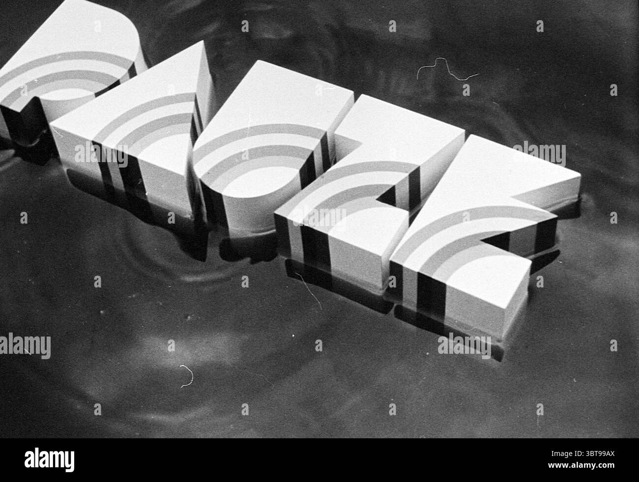 Registrazione TV "PAUSA" televisione, Whizgle News, Dutch Desk, Paesi Bassi, 1950 - 2000 il 28-05-1976. Questi argomenti sono mostrati nell'immagine. La scena presenta una composizione dinamica incentrata su una serie di forme a incastro che ricordano lettere o forme, presentate in uno stile elegante e moderno. Queste forme sono colorate in una tavolozza di bianco, varie sfumature di grigio e delicate sfumature di pastello, che ne esaltano l'atmosfera contemporanea. Posizionate su una superficie riflettente, le forme creano riflessi intriganti che distorcono e ondulano mentre interagiscono con l'acqua sottostante, suggerendo movimento e fluidità. Foto Stock