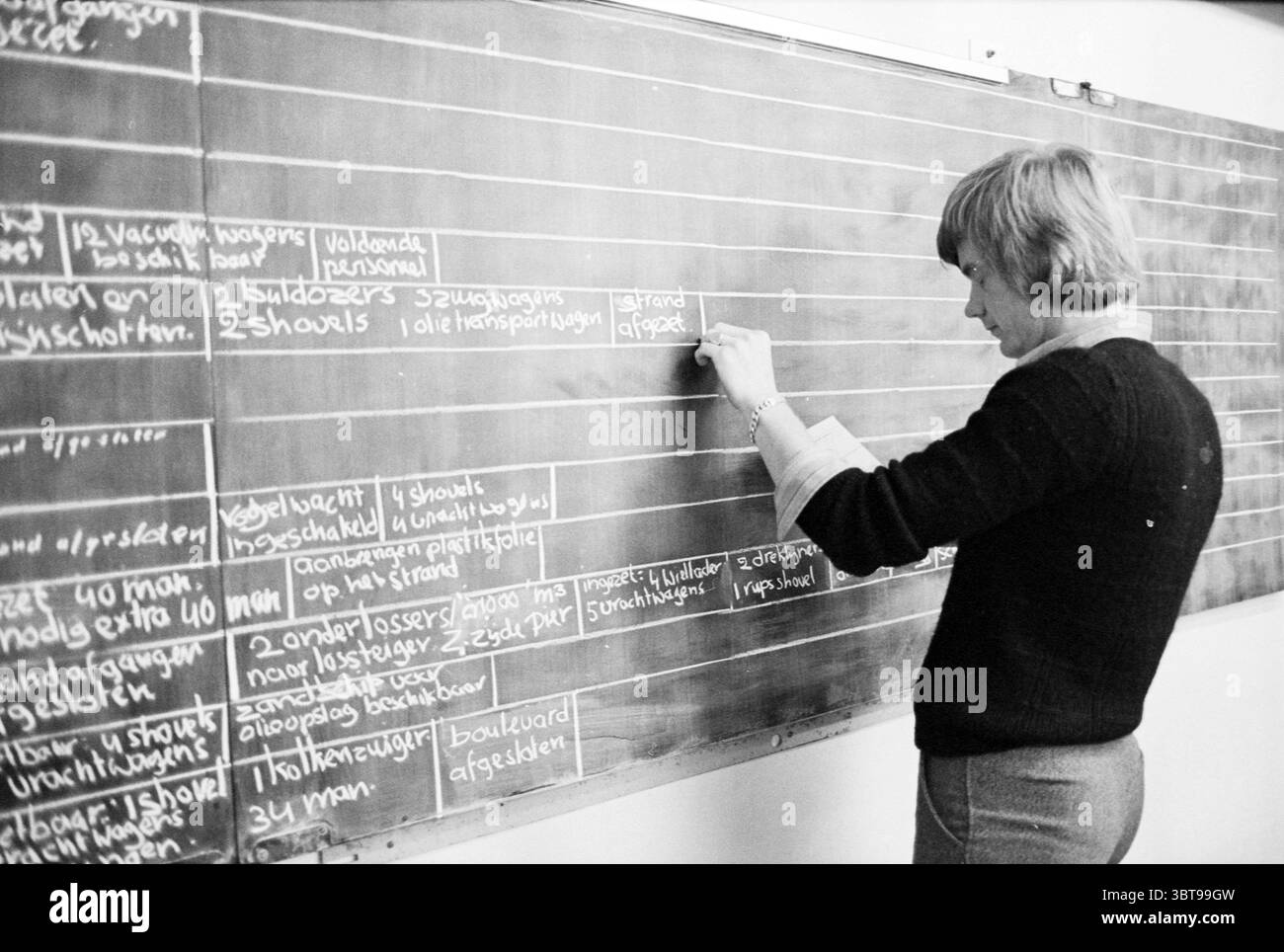 Azione del piano di catastrofe dopo i disastri causati dagli incidenti del Mare del Nord, Whizgle News, Dutch Desk, Paesi Bassi, 1950 - 2000 il 08-10-1979. Questi sono gli argomenti nell'immagine. In un ambiente di classe, una donna si trova accanto a una grande lavagna piena di scrittura di gesso. È impegnata a scrivere o cancellare qualcosa sul Consiglio, indicando un momento di insegnamento o di istruzione. La donna ha capelli corti e di colore chiaro ed è vestita con un maglione nero, che contrasta con le pareti bianche intorno a lei. La lavagna è il punto focale della scena, con varie righe di testo scritte in gesso bianco, che mostrano diff Foto Stock